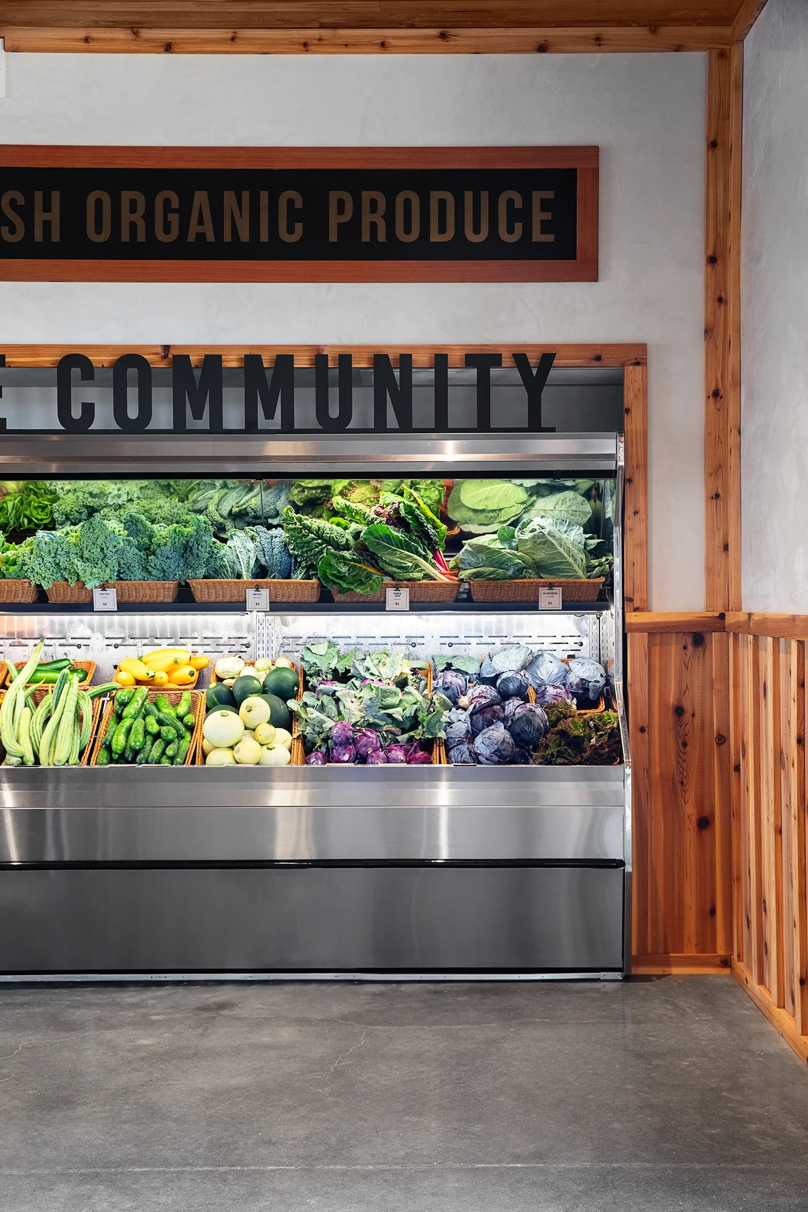 Refrigerated produce case below fresh organic produce signage in the Fox Point Farms market hall