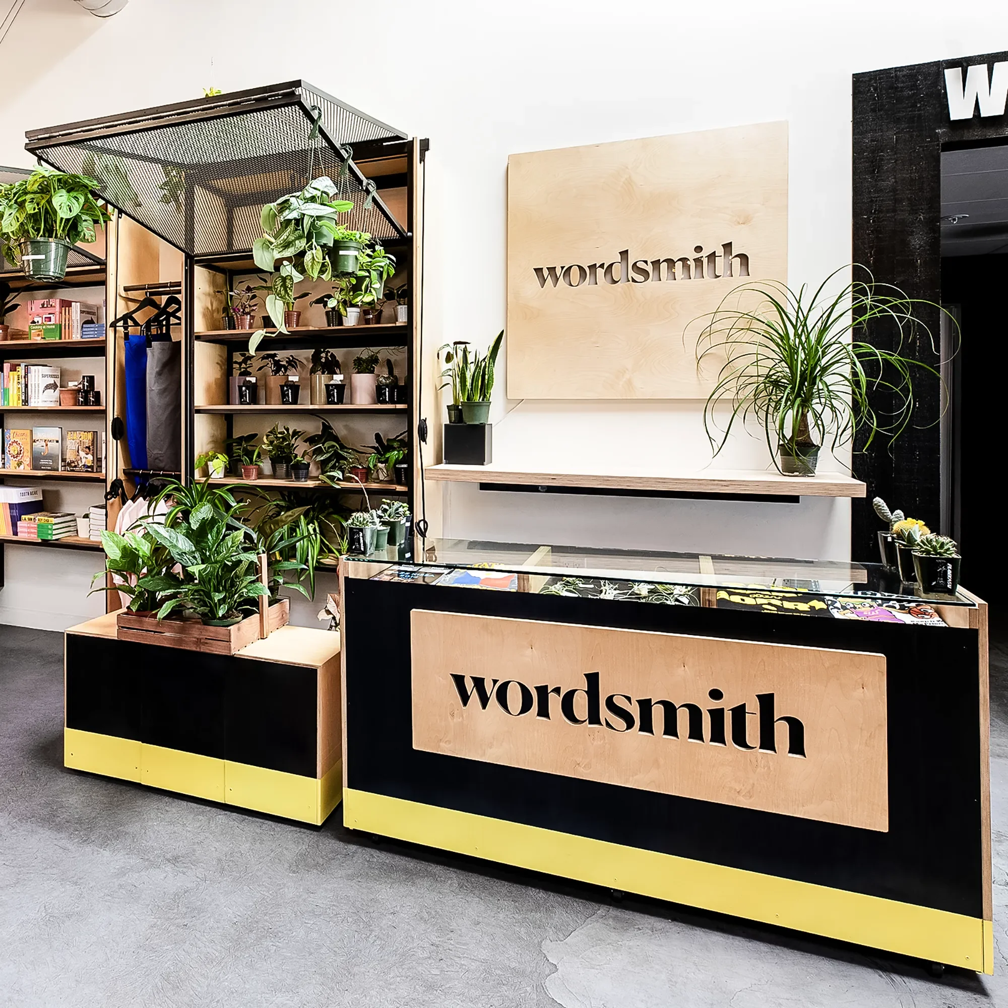 Custom point of sale counter with a yellow base and printed wordmark panel with display shelving behind at Wordsmith