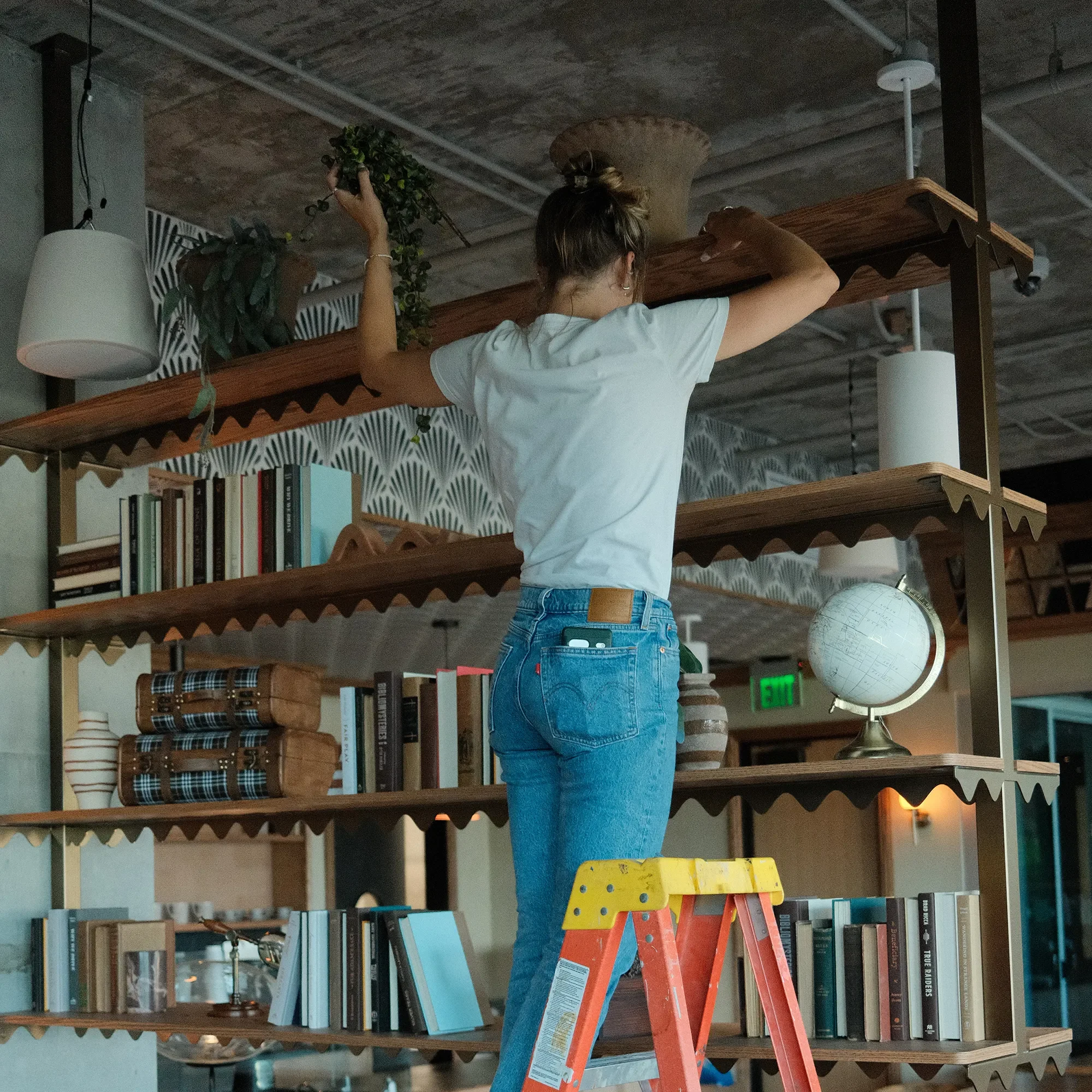 Interior designer from Tecture Studio placing books and ceramics on suspended wooden shelves during a furniture install