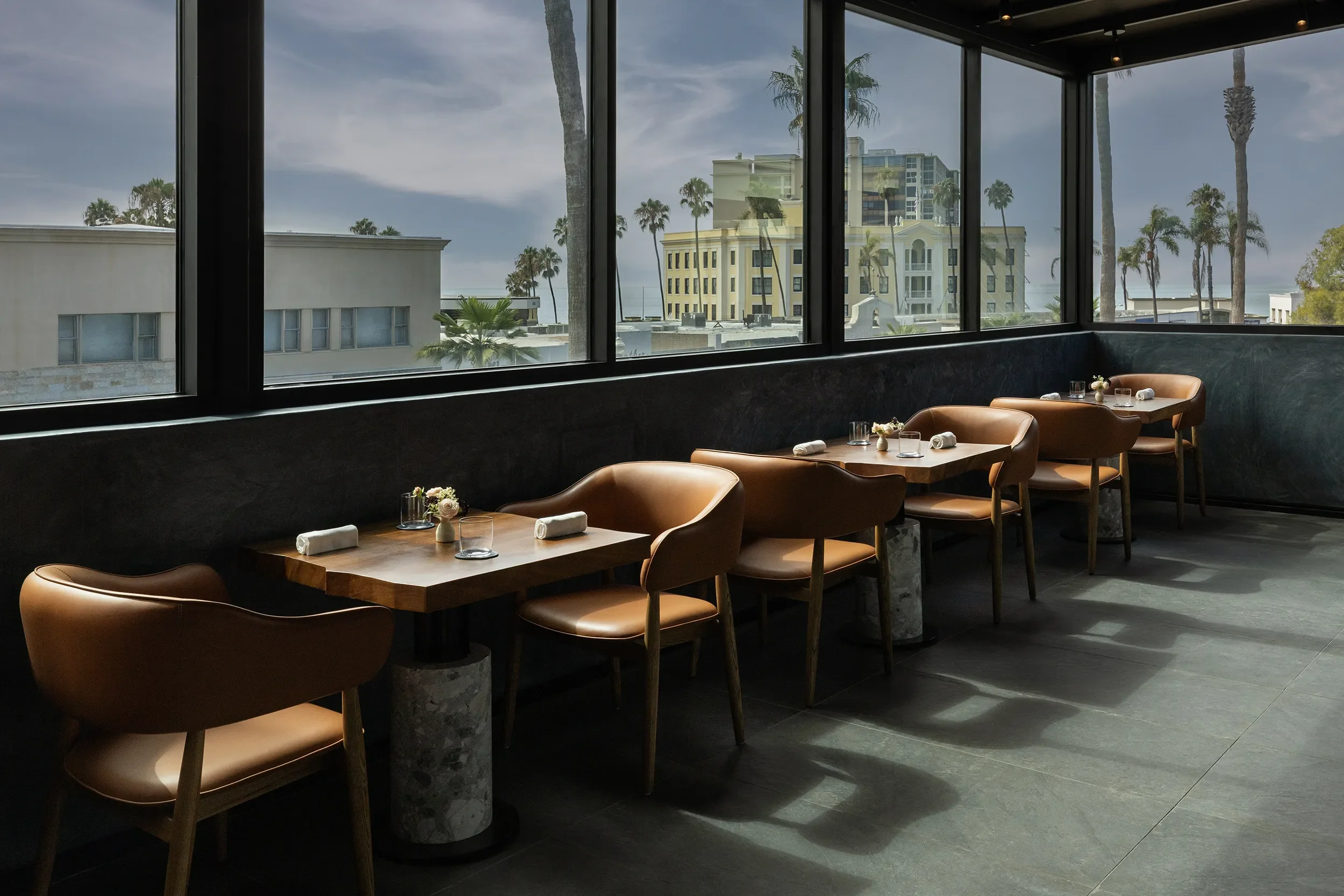 Row of window-side tables with a view of the ocean and palm trees at Lucien in La Jolla