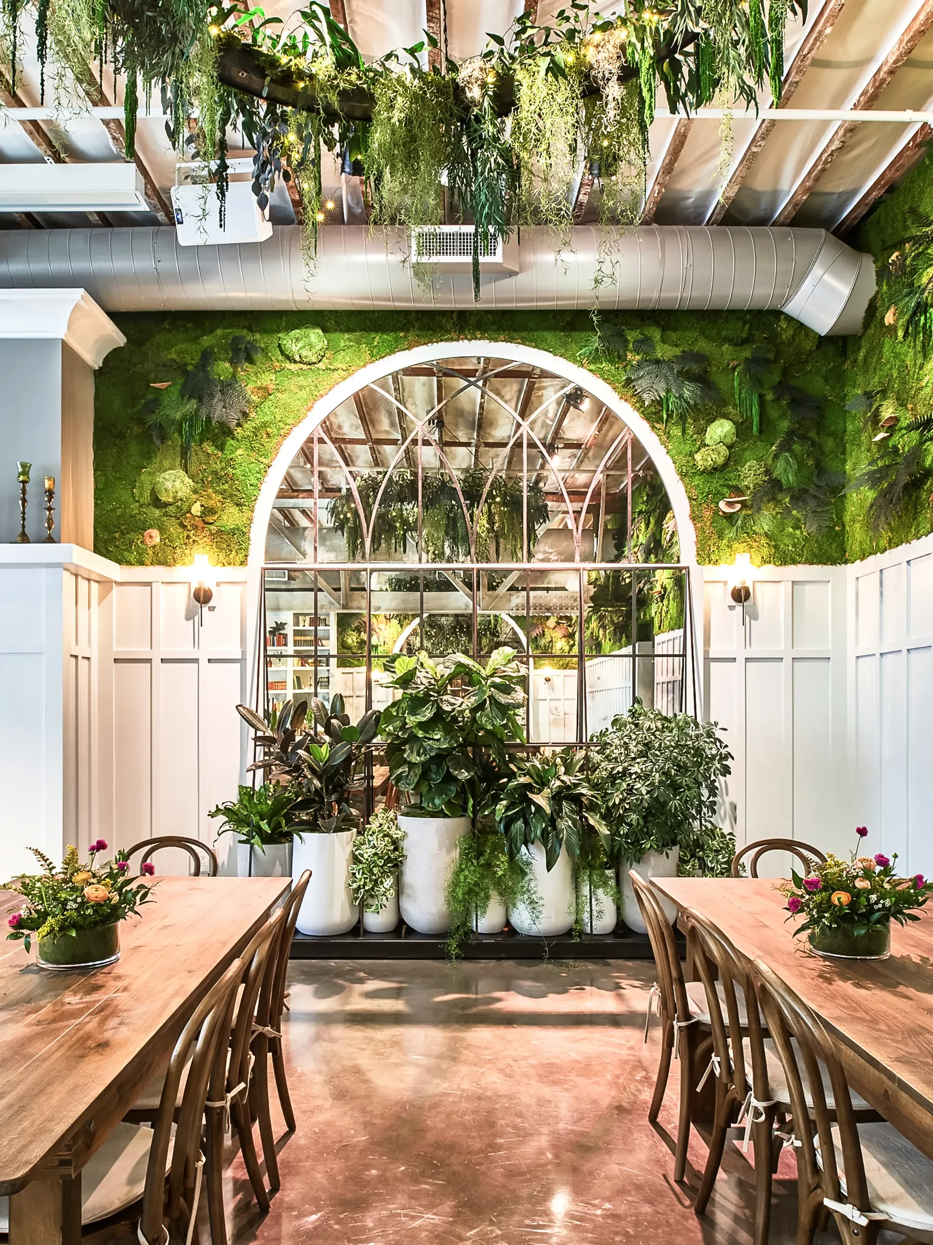 Planted archway framing timber communal tables in the event space at Flora The Venue