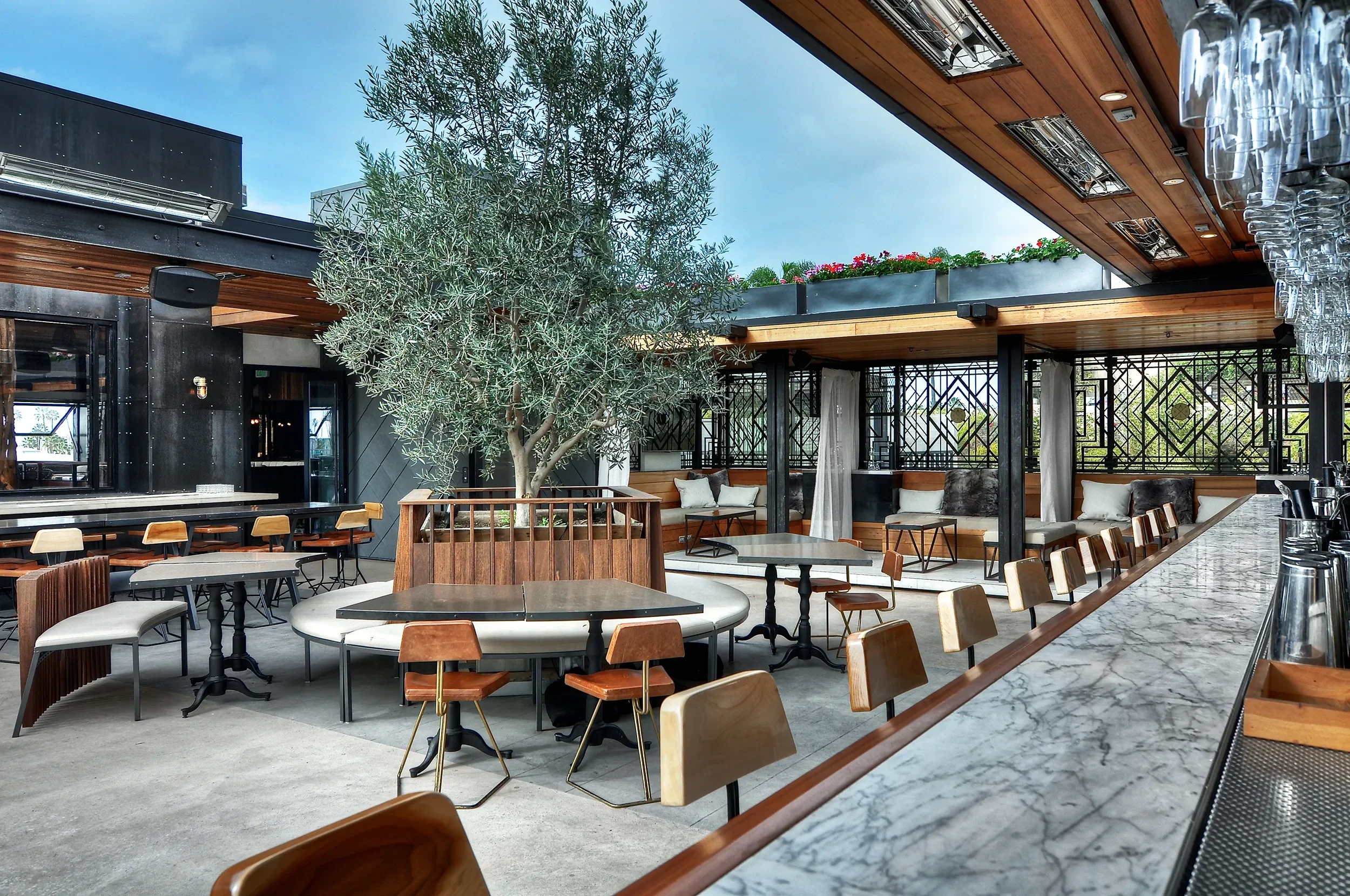 Covered patio with communal tables and a marble bar under an olive tree at Kettner Exchange, Little Italy
