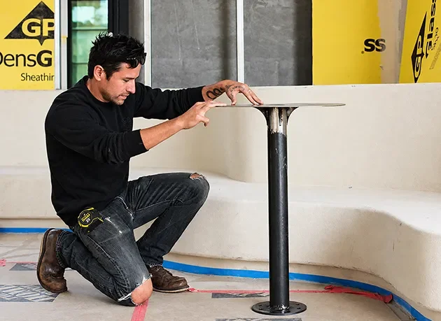 Installer fitting a table base beside a plaster banquette during construction administration.