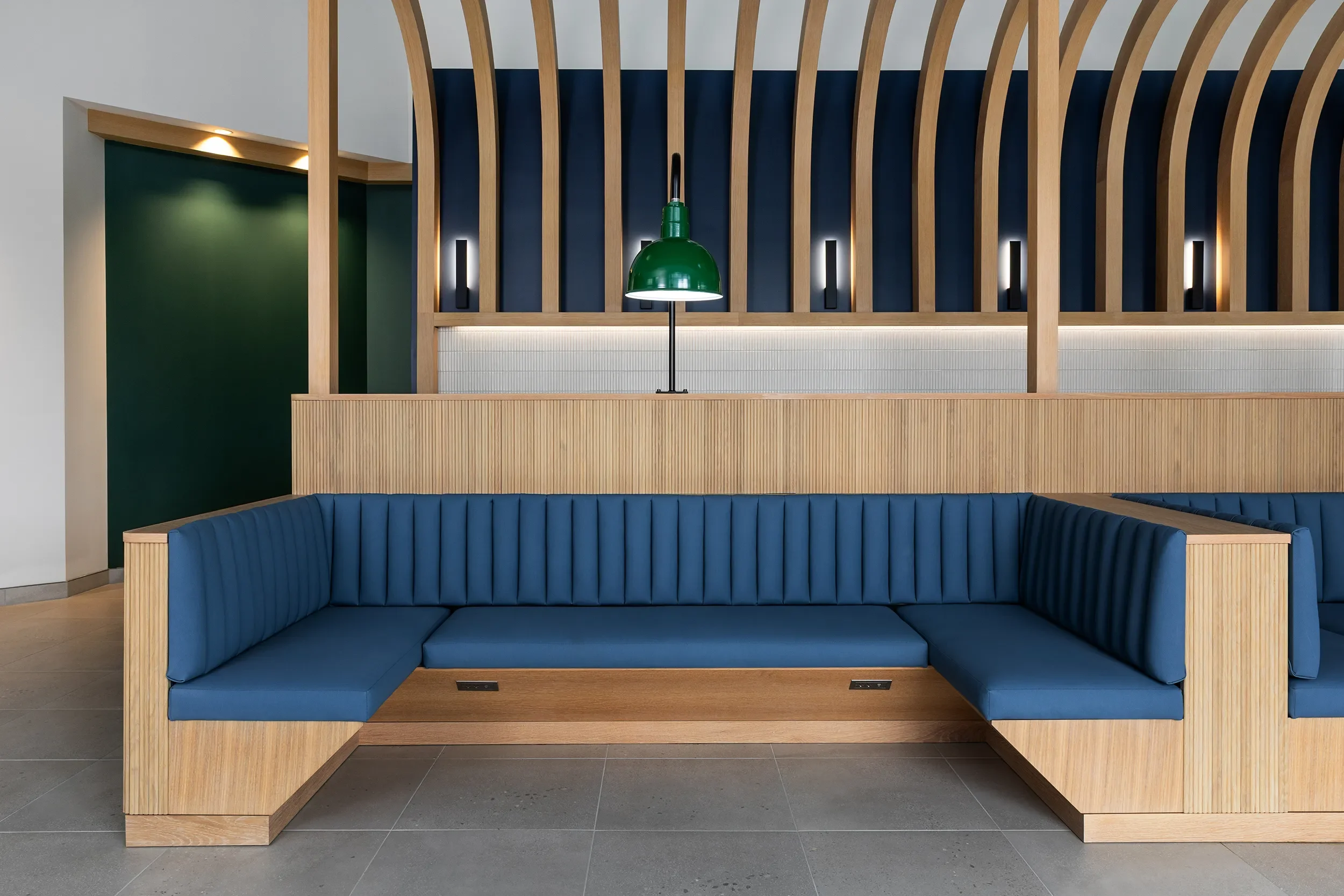 Custom blue upholstered booth seating with a curved wood slat overhead structure attached to the back in a San Diego office