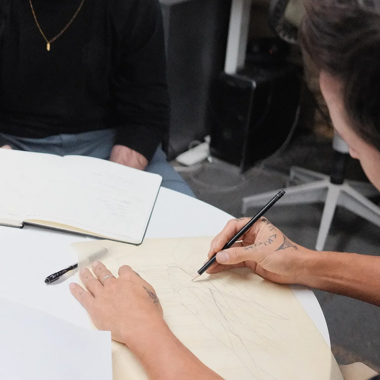 Hand sketching a detail on trace paper over a drawing set