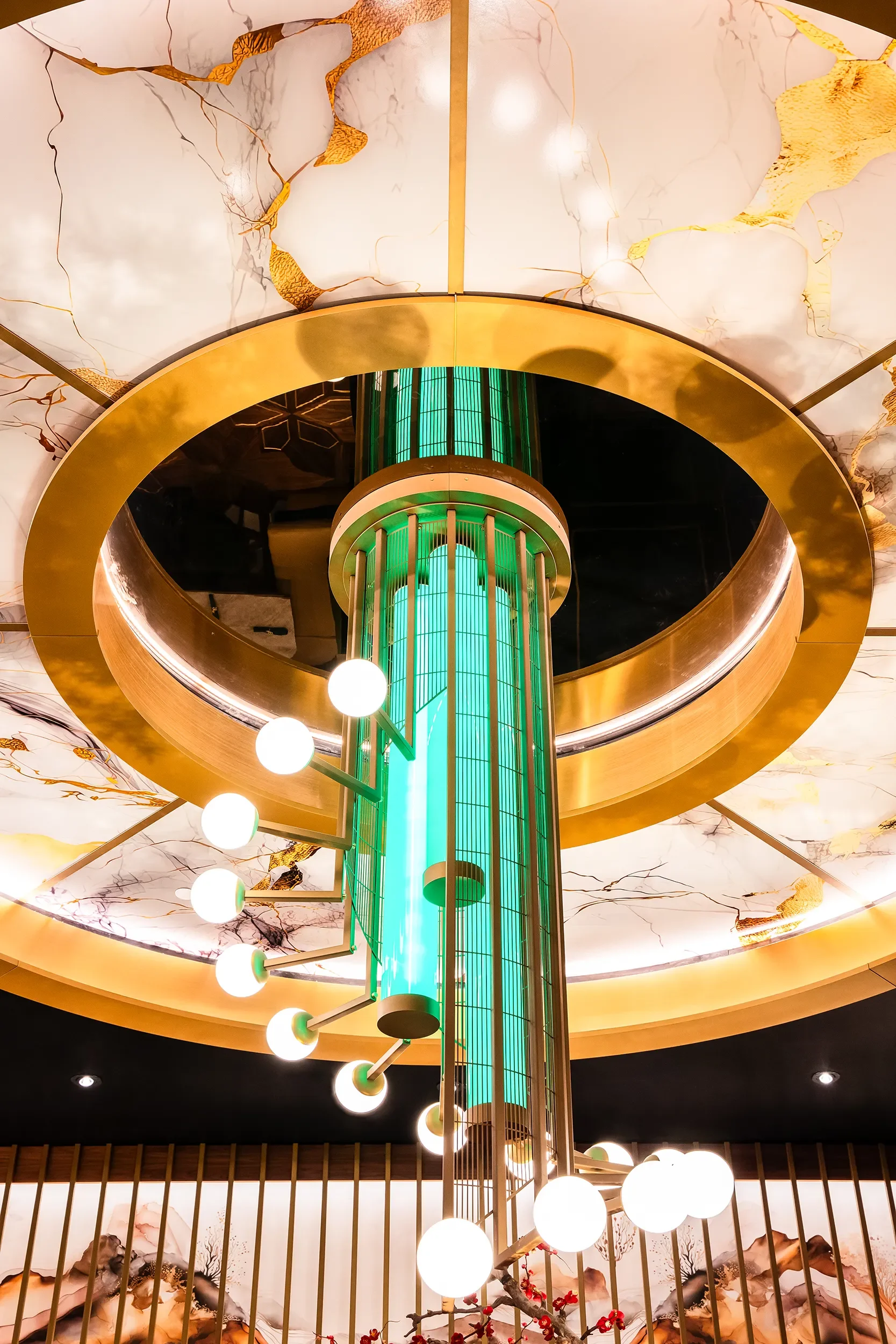 Custom sculptural chandelier with bronze rods, globe lighting, green lit center tubing, and marble ceiling surround, suspended over booth seating at Emerald at Jamul Casino