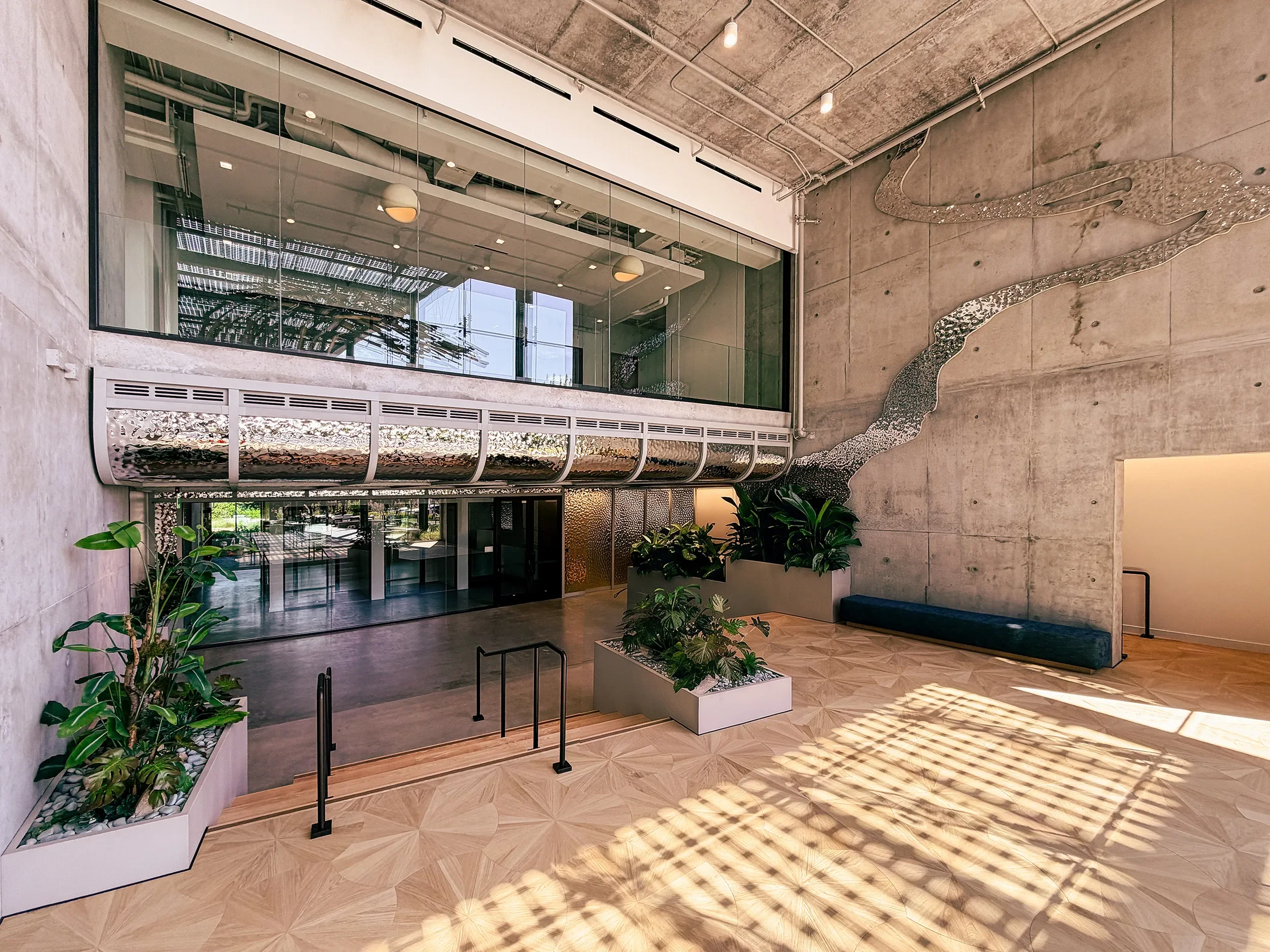 Rippling perforated metal ribbon running along a mezzanine edge and up a concrete lobby wall