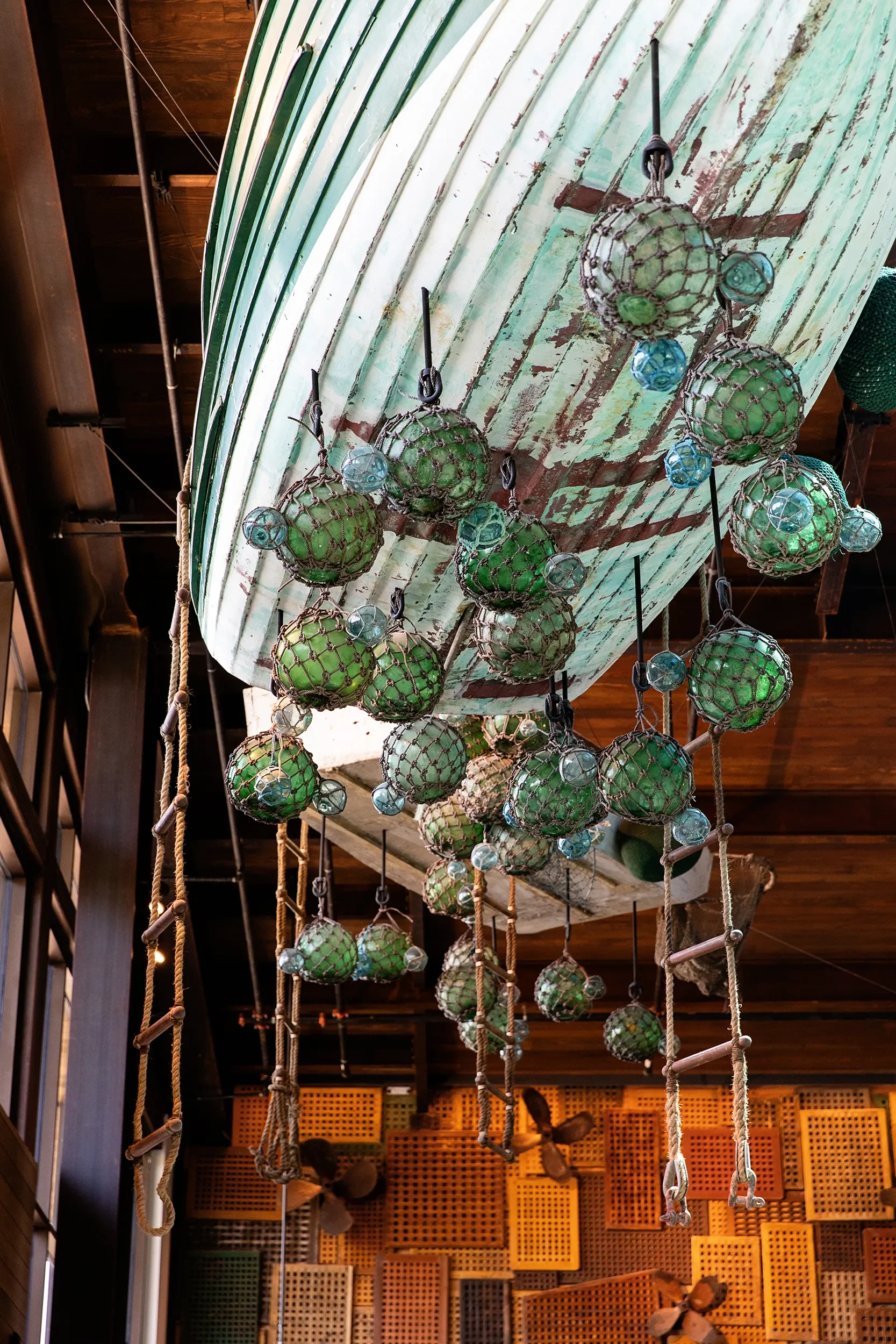 Upturned wooden boat hull suspended above the bar with clustered glass floats at Skydeck in Del Mar