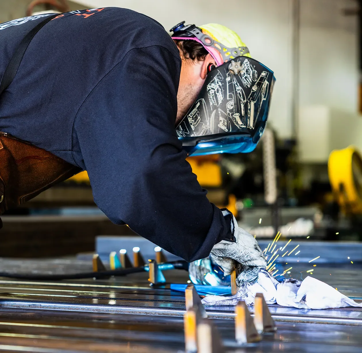 Fabricator welding a steel assembly with sparks flying in the Tecture AF shop.