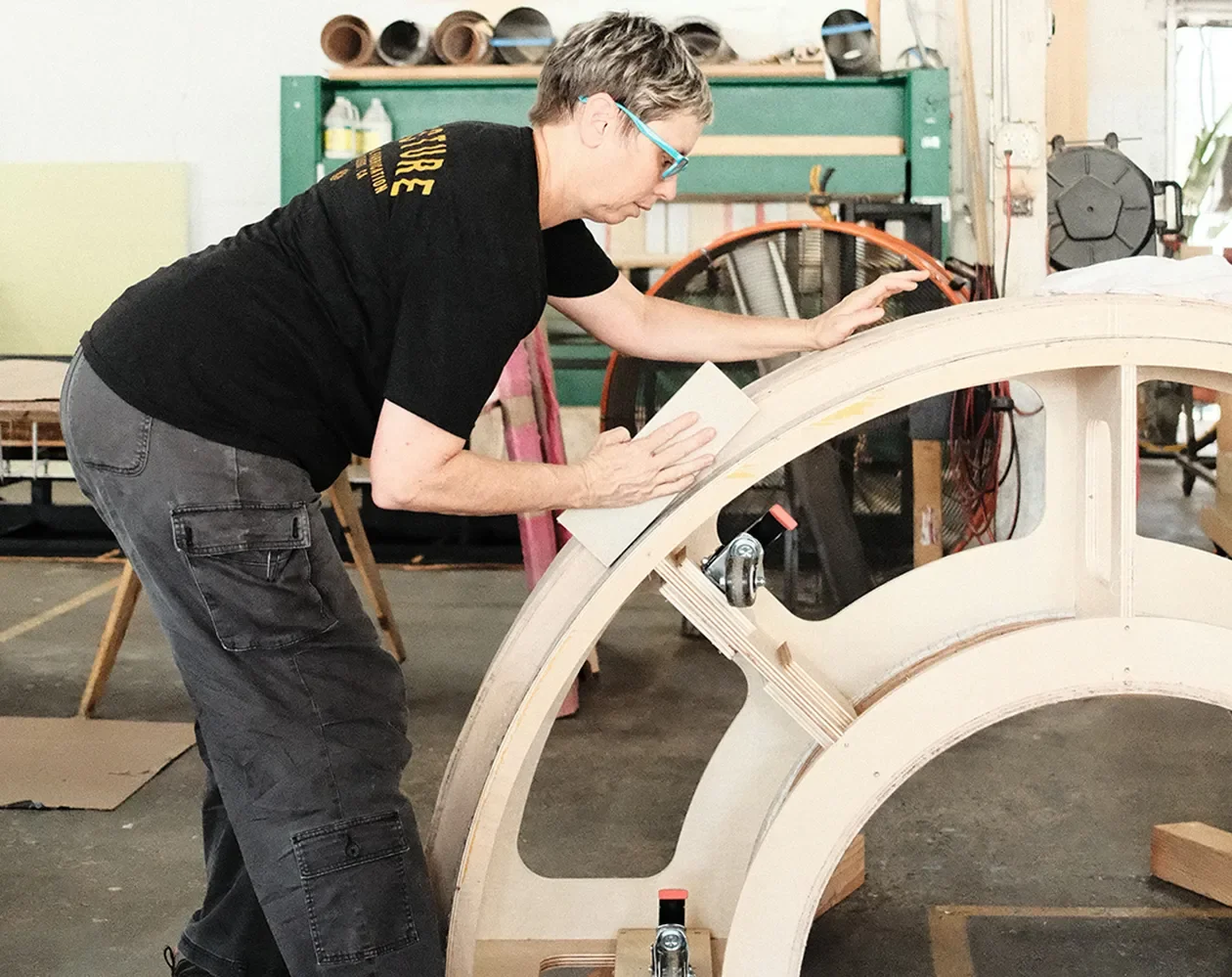 Fabricator hand-finishing a curved plywood arch in the Tecture shop.