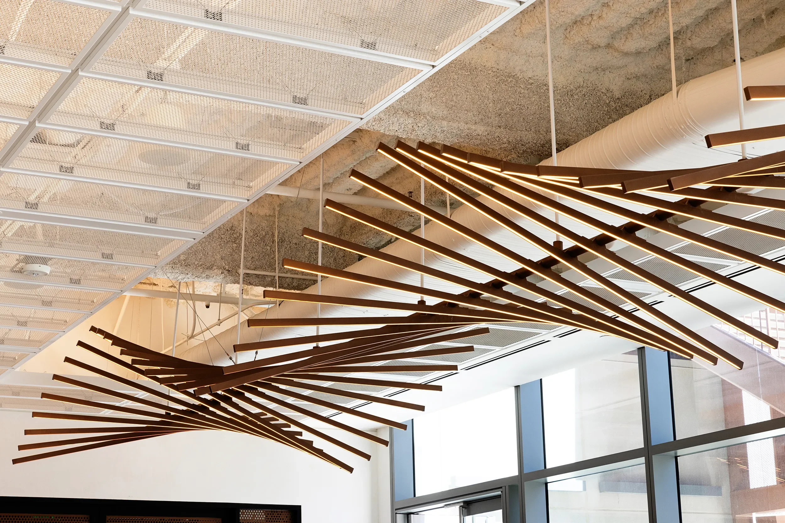 Custom large sculptural light fixture made of bronze rods undulating to create movement, suspended in a large lobby space 