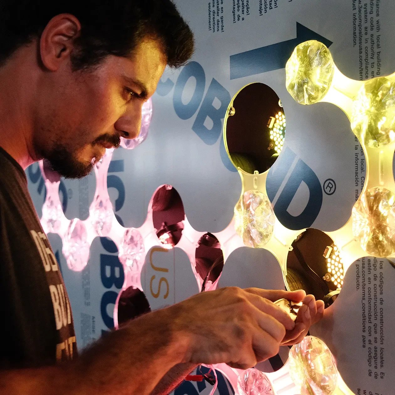 Fabricator assembling a backlit panel with glowing organic openings in the shop