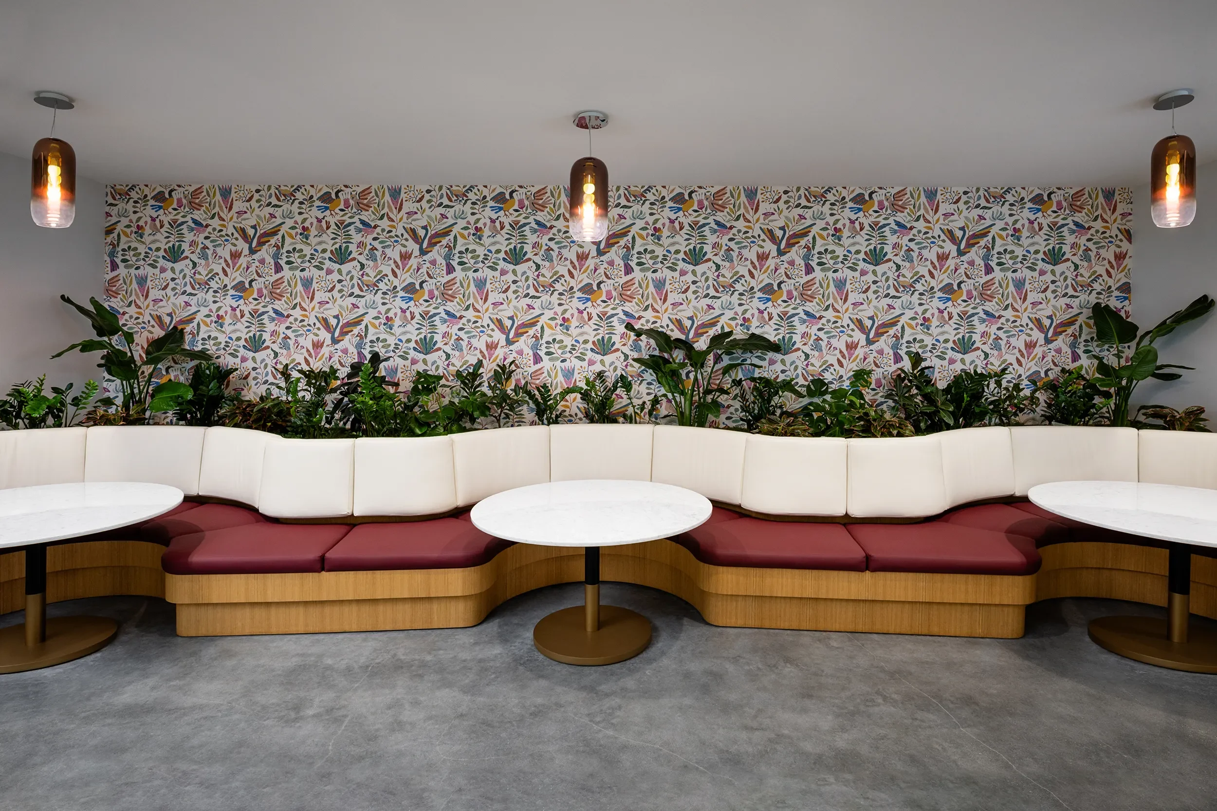 Curved custom banquette with burgundy cushions and round cafe tables beneath a floral wallpaper in Torrey Pines San Diego