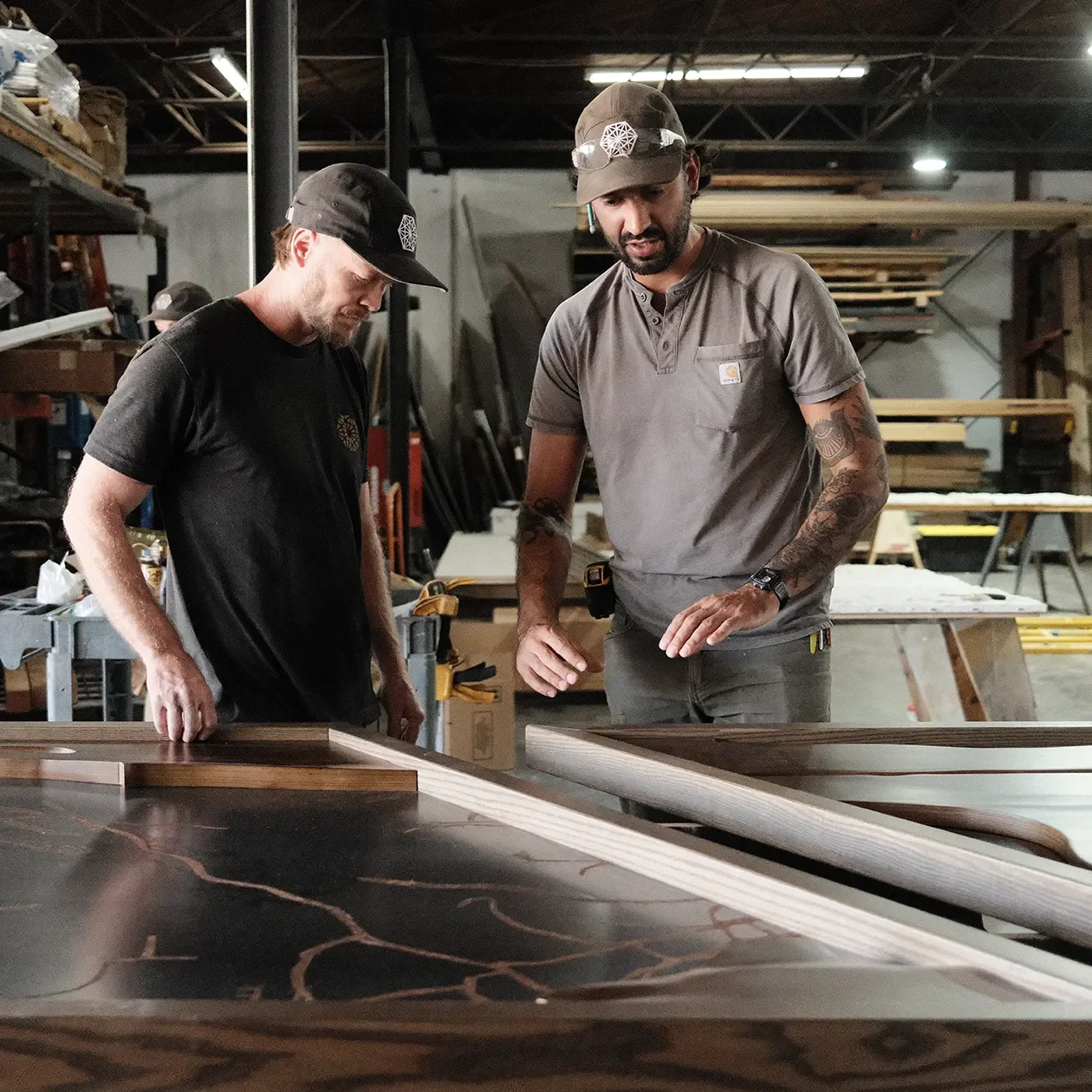 Two fabricators reviewing a large etched metal art panel on the bench in the shop