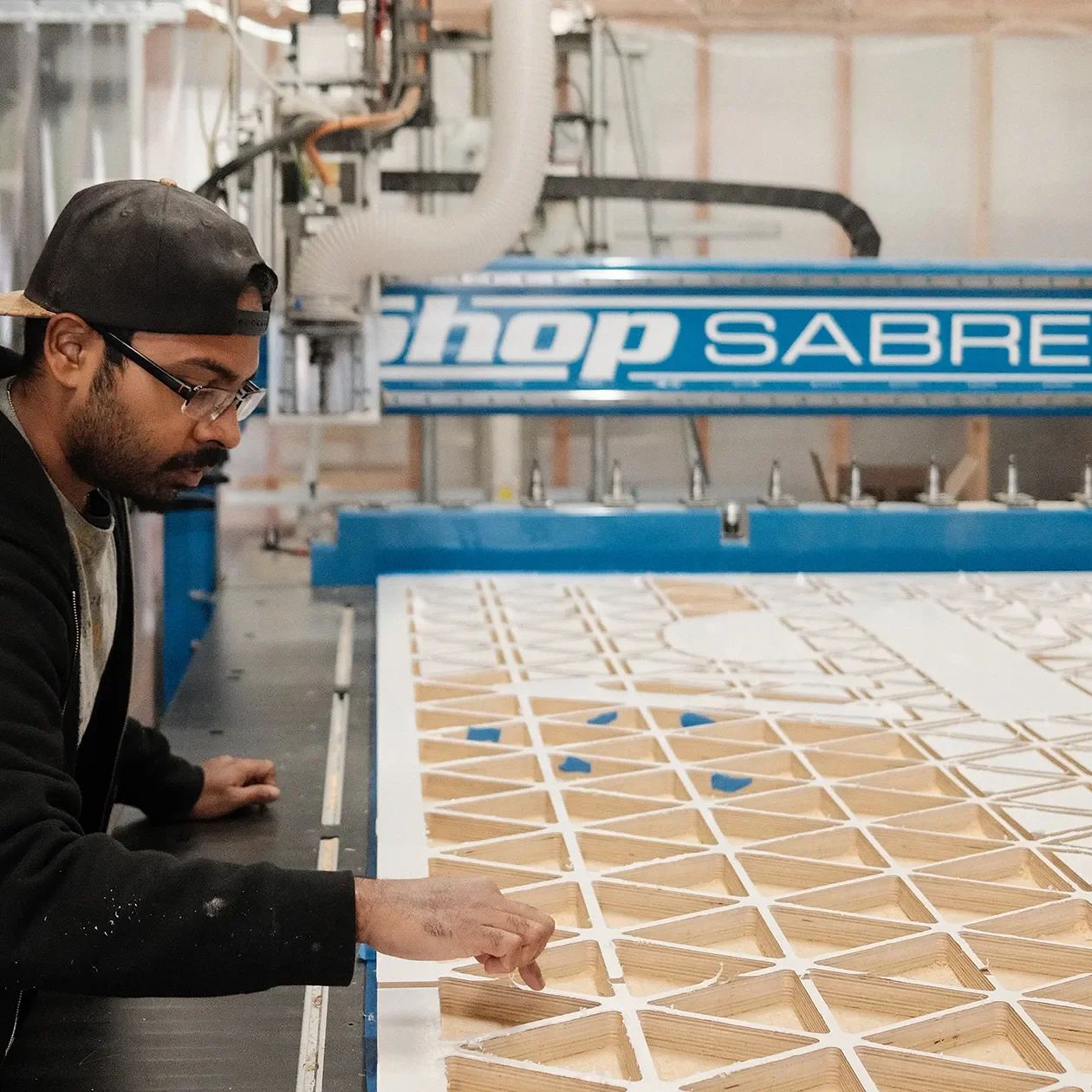 Fabricator at the CNC router clearing a routed lattice panel at the Tecture shop in San Diego