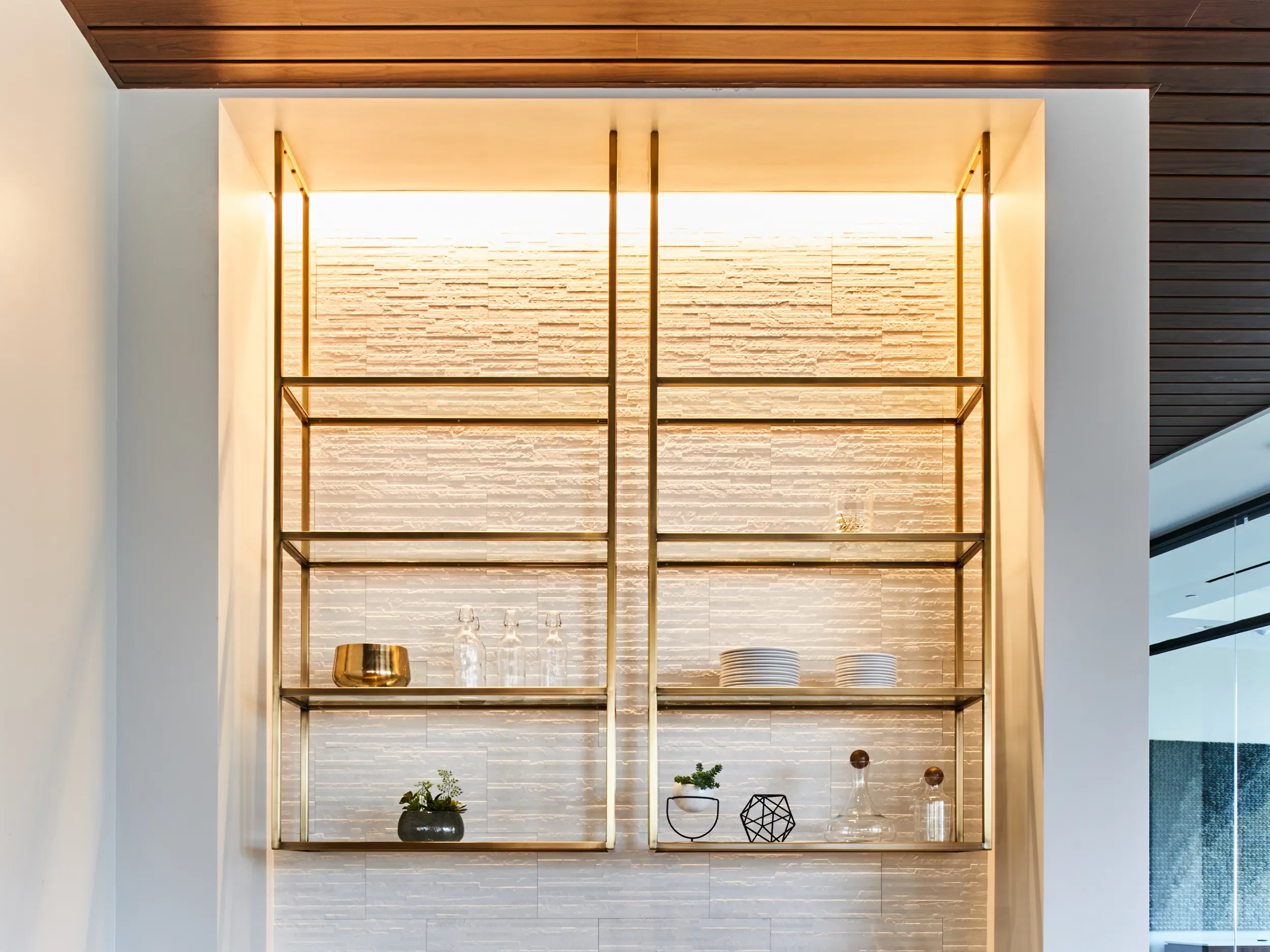 Custom suspended brass display shelving with integrated lighting against a textured stone wall