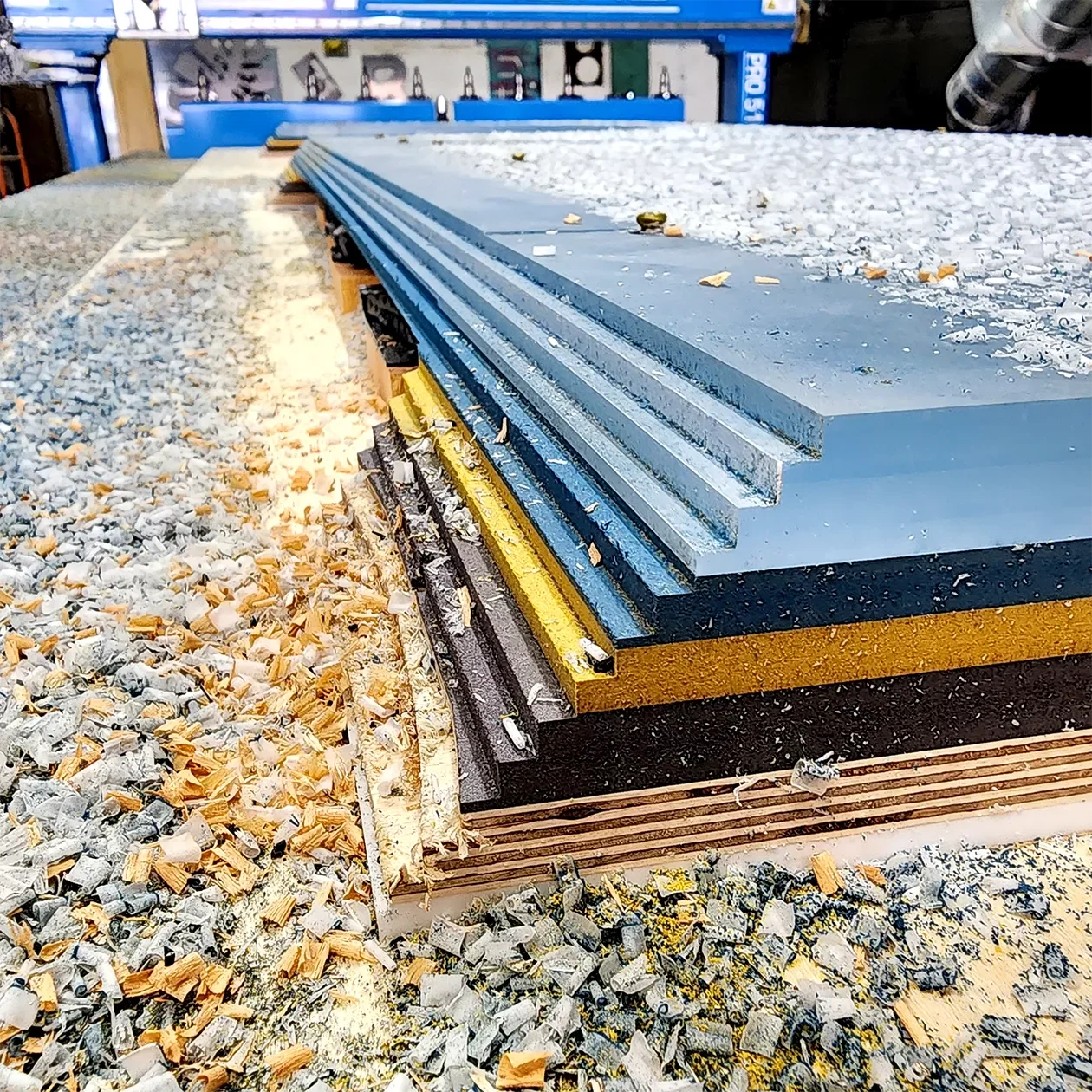 Stack of colored MDF panels on the CNC router bed among cut chips being used for a material study