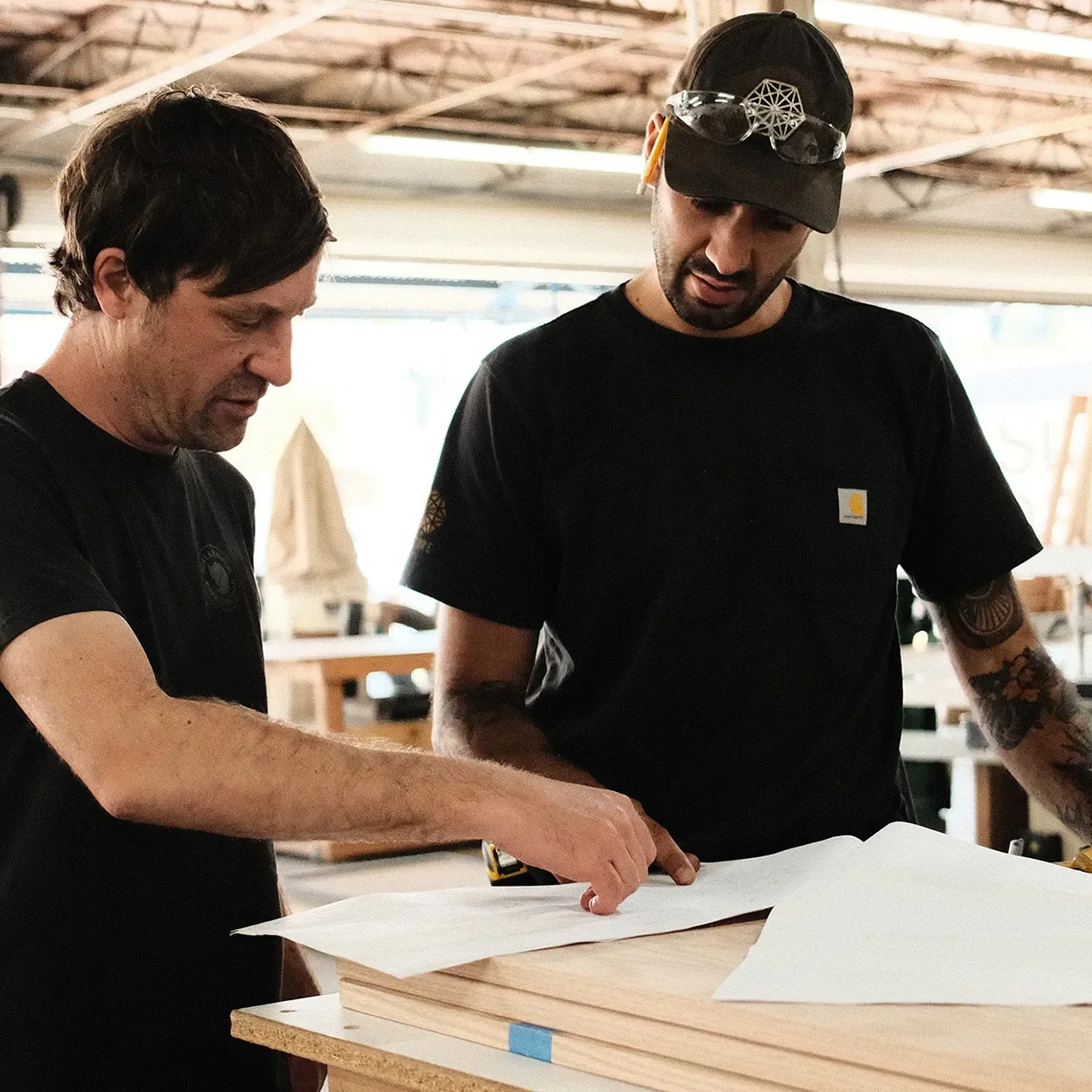 Two fabricators reviewing a drawing over sheet stock on the shop floor