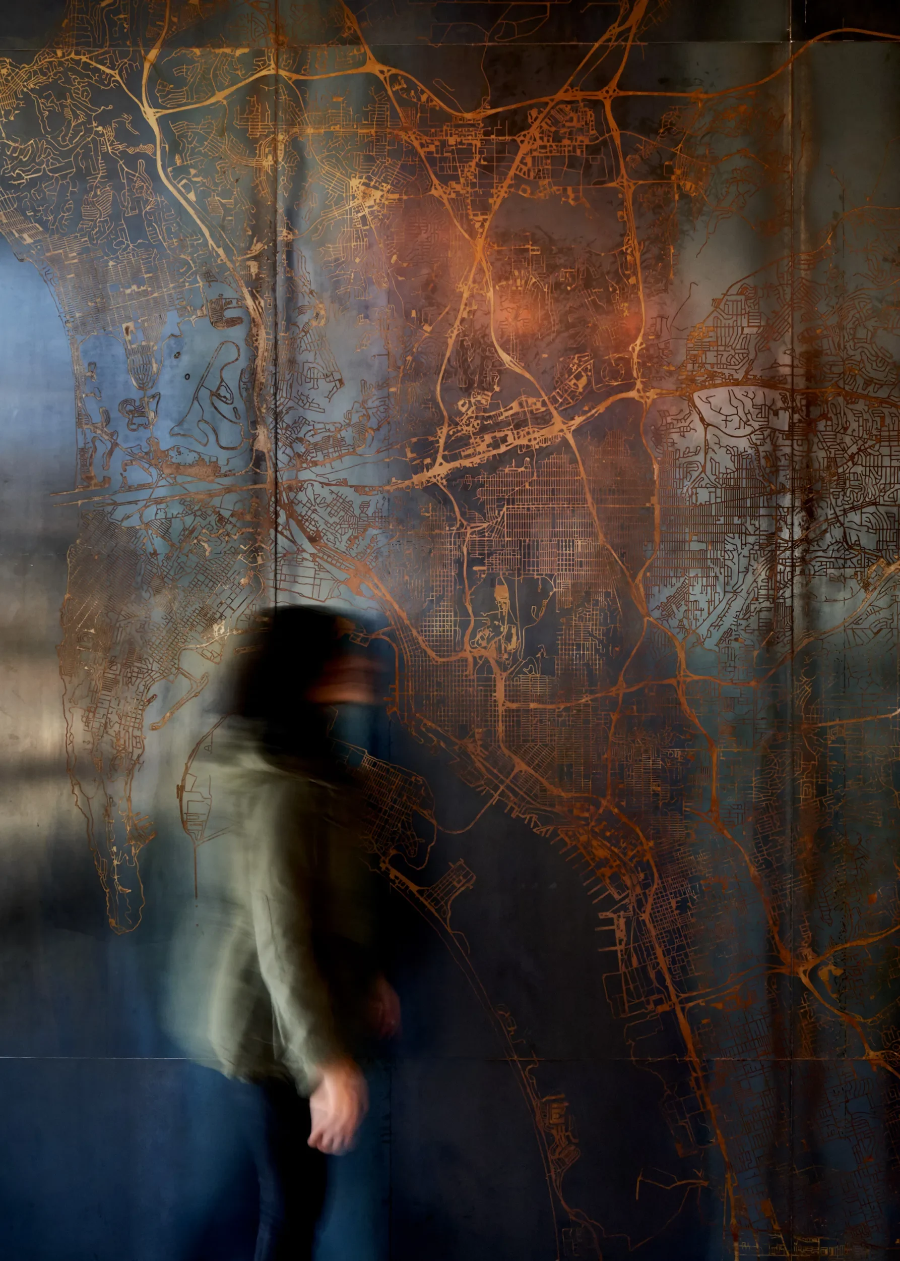 Acid etched steel map panel with a person walking past, the Rust Map installation in San Diego