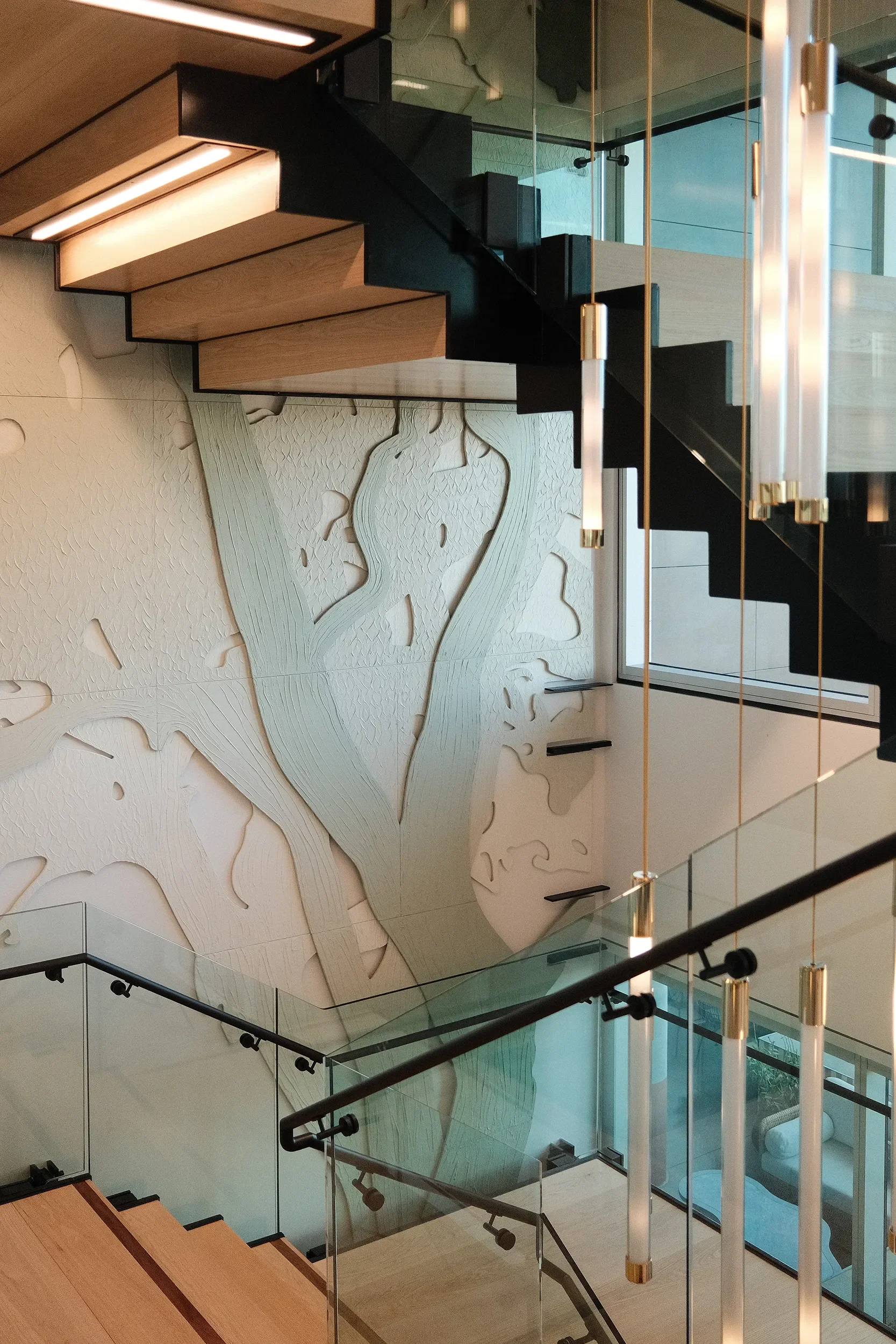 Carved relief wall of branching forms alongside a floating stair with a glas balustrade