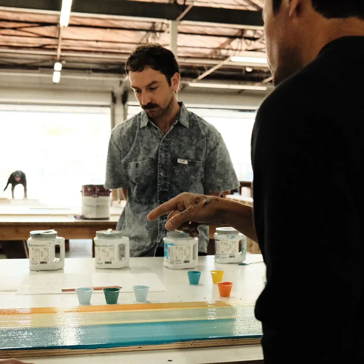 Two team members reviewing finish samples and a painted mockup panel on the shop floor