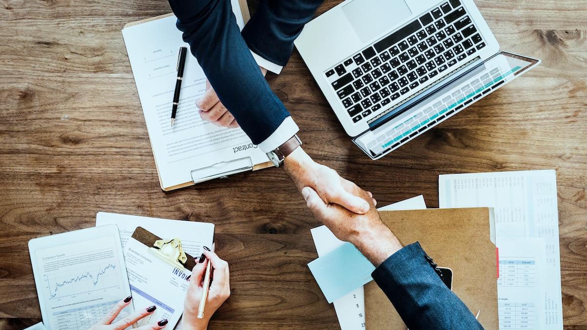 birdseye view of a handshake over a laptop and professional looking documents