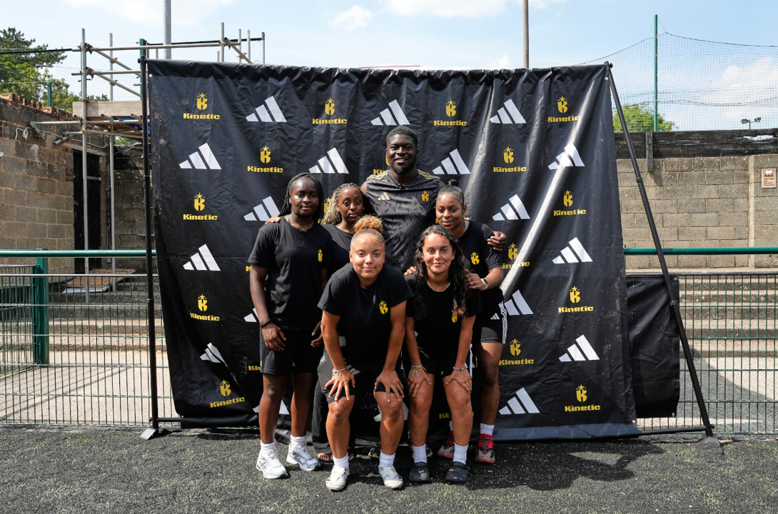 A group of Kinetic students posing in front of a Kinetic Foundation and adidas branded backdrop