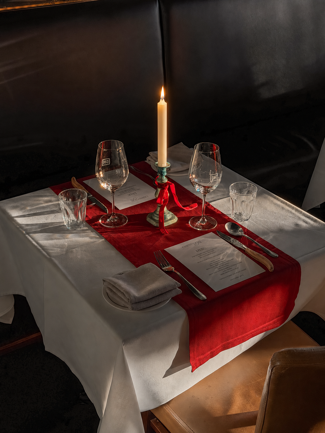 A Christmas place setting with a red runner, wine glasses and a candle
