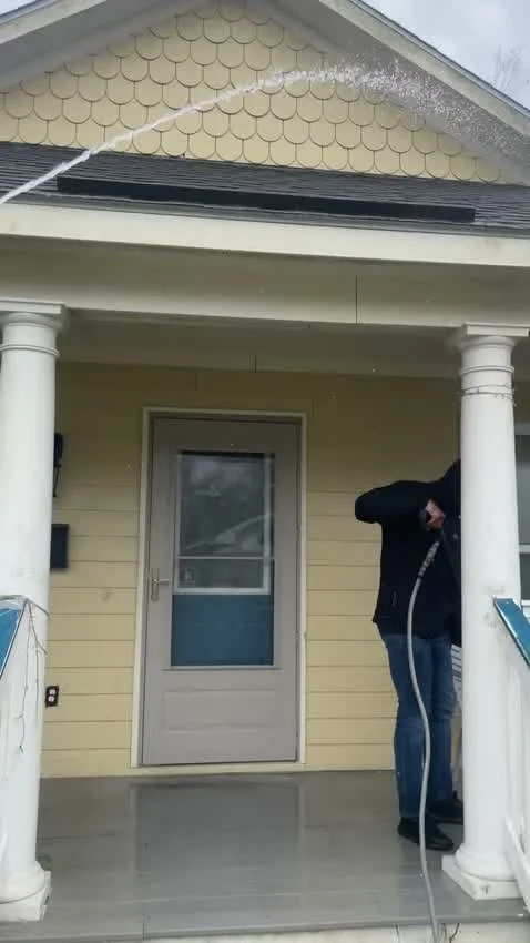 Soft-washing a house gable, water arc visible