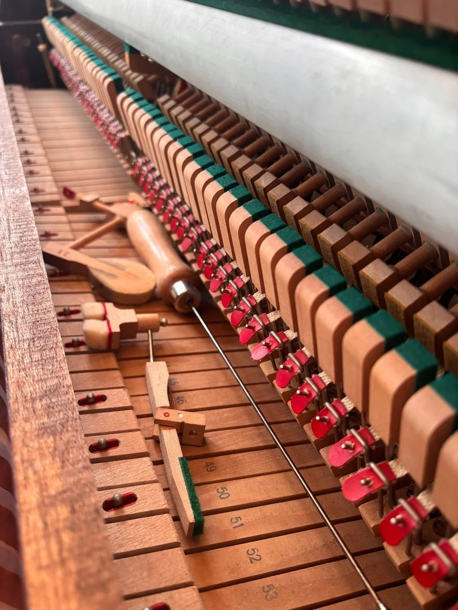 Upright piano action with tools and removed components during servicing.