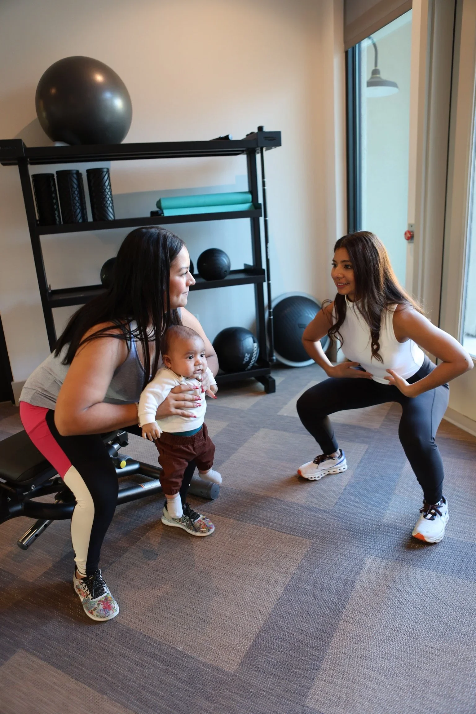 A postpartum patient holding her baby while Christine guides a squat at The Pelvic Lab