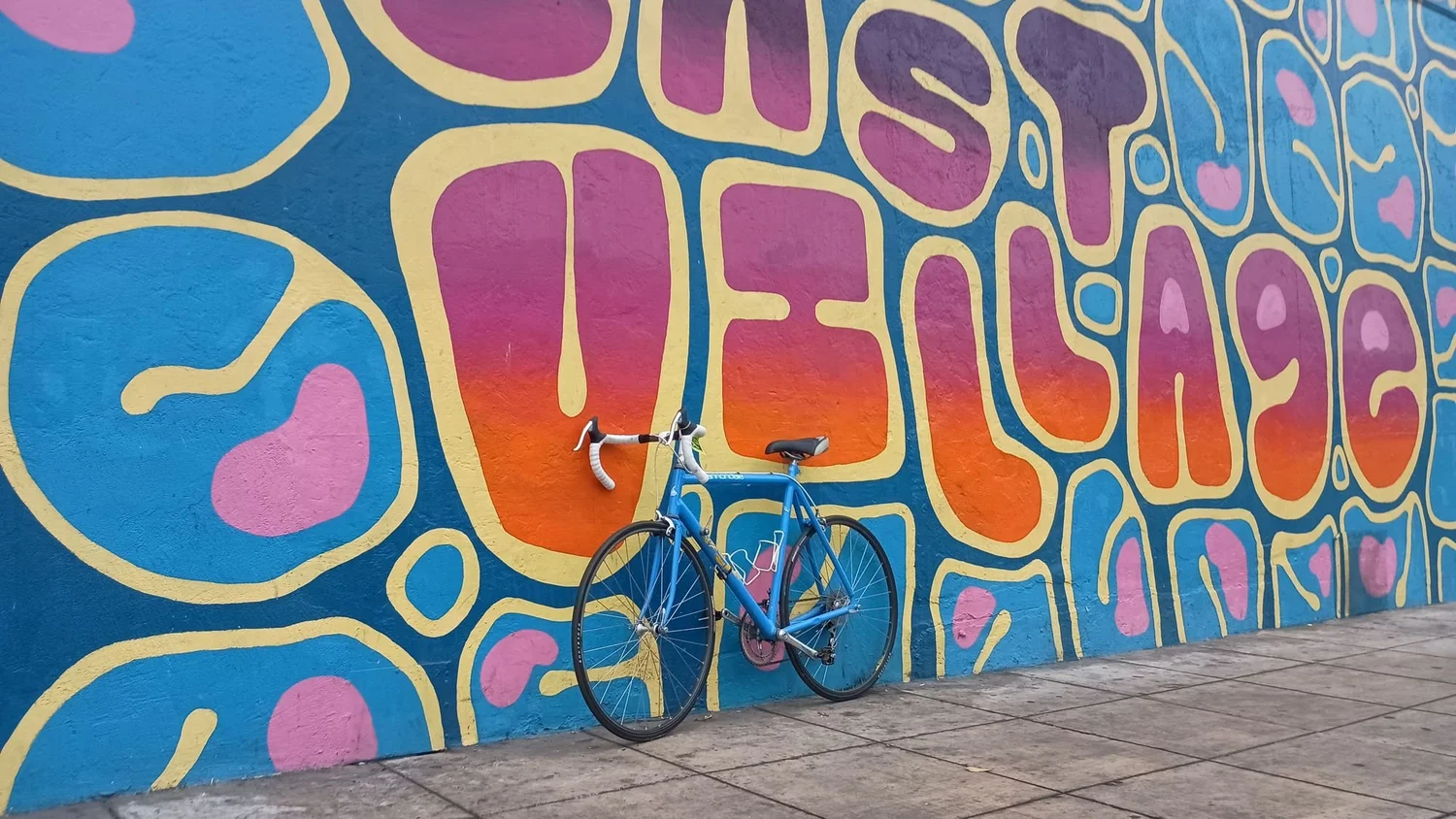A blue road bike leans against a bright East Village mural