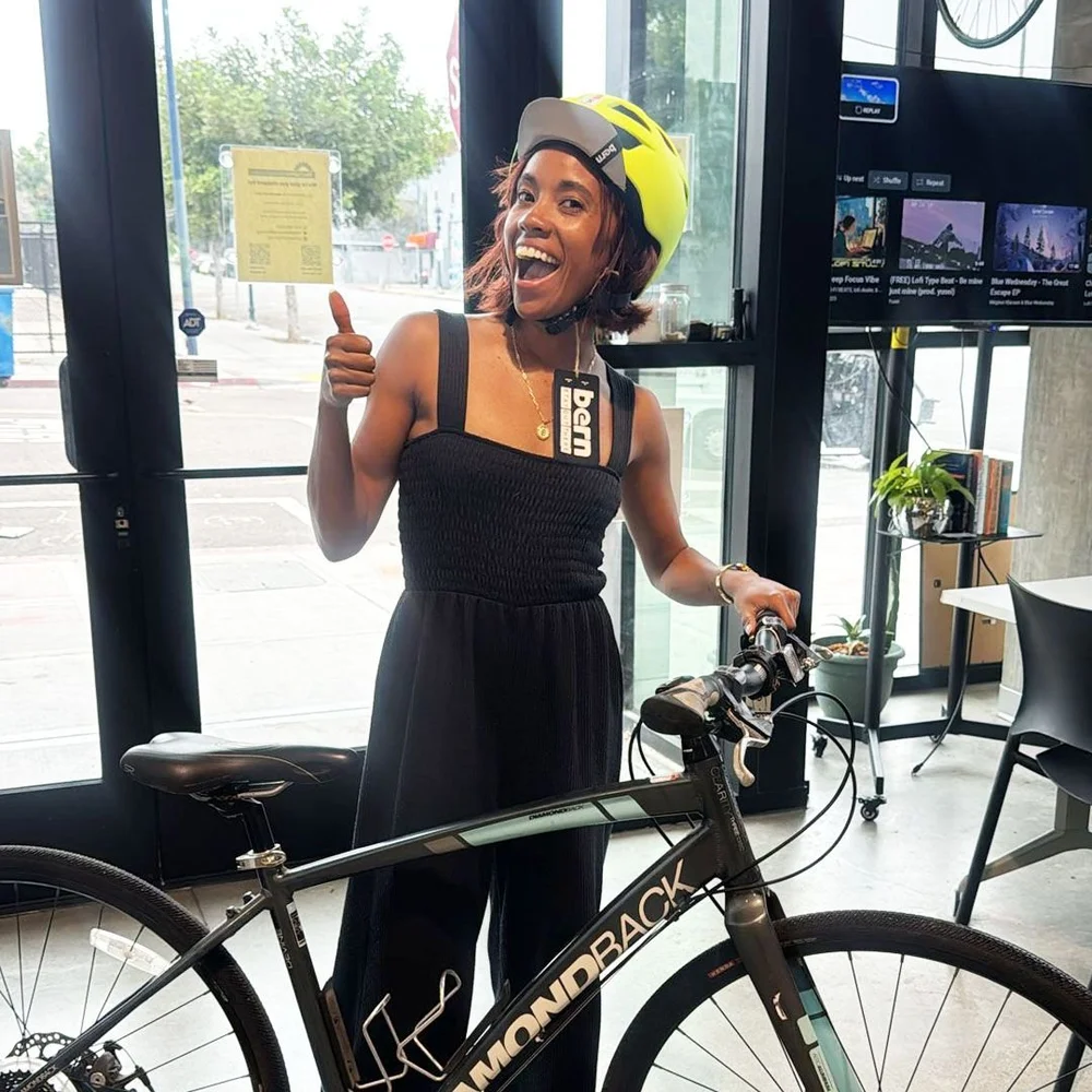 A new rider in a yellow helmet gives a thumbs up beside her bike