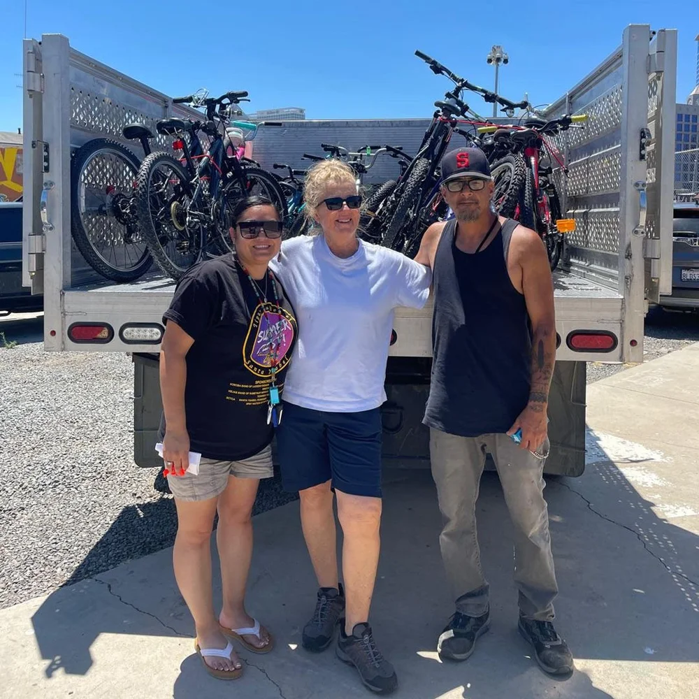 Three people stand in front of a truck bed loaded with bikes