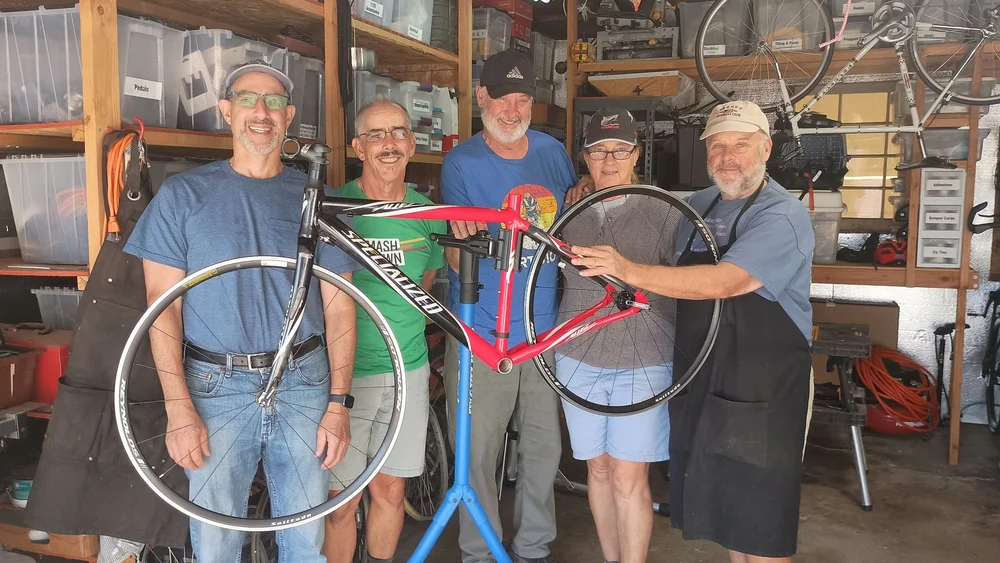 ReBikeSD volunteers hold up a red road bike in the workshop
