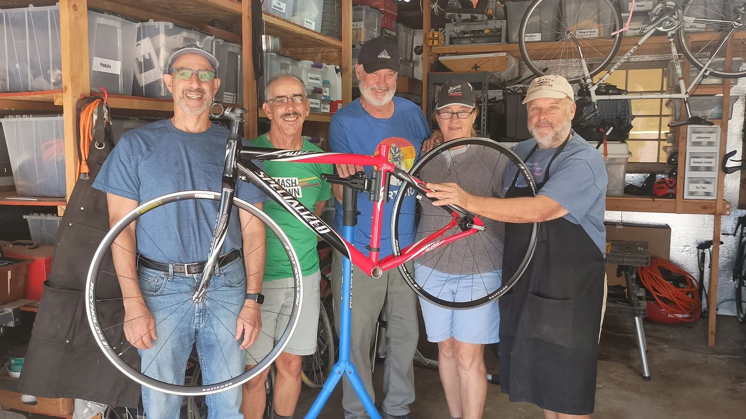 ReBikeSD volunteers hold up a red road bike in the workshop