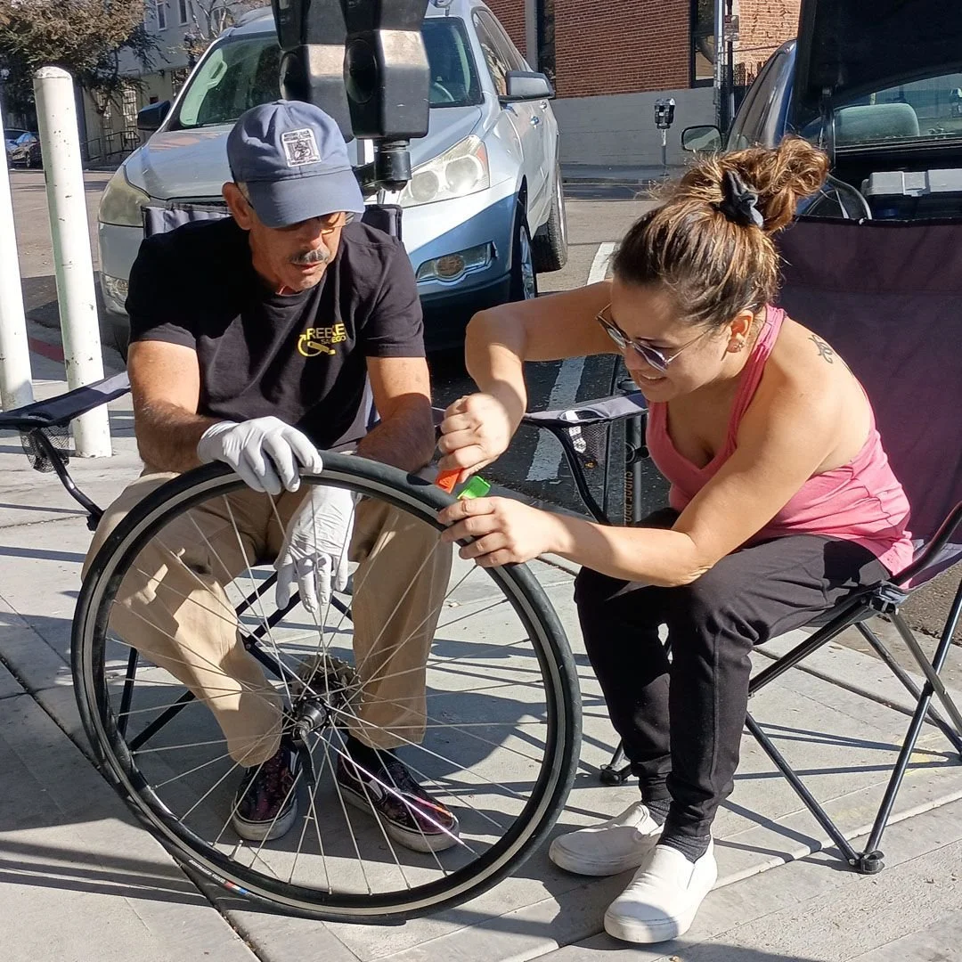 A volunteer mechanic shows a rider how to seat a tire