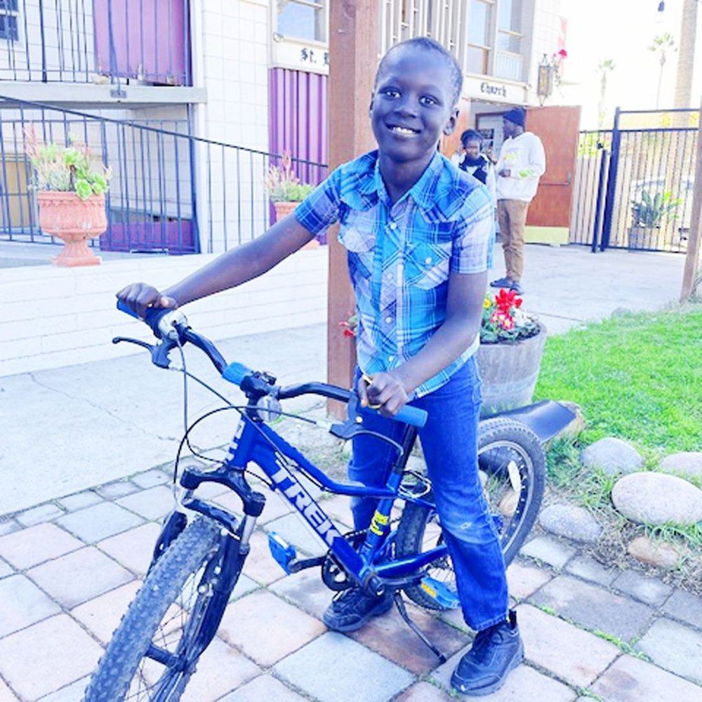 A boy smiles on a blue bike at a community repair event