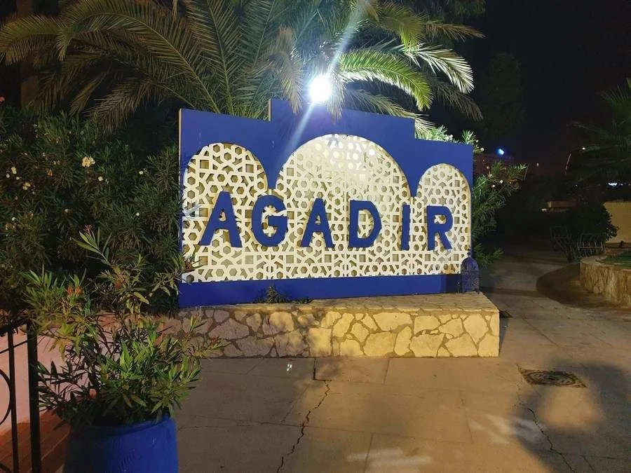 L’enseigne lumineuse AGADIR en lettres bleues sur un mur blanc de style mauresque, la nuit, à l’ancien Club Med Agadir (Maroc)