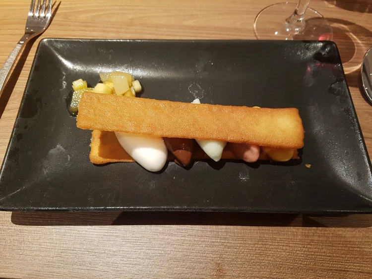 A plated dessert: a long biscuit over scoops of sorbet and ice cream, with diced fruit