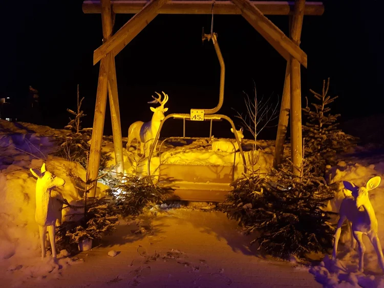 A vintage chairlift seat, number 45, set in the snow with deer figures and lit up at night