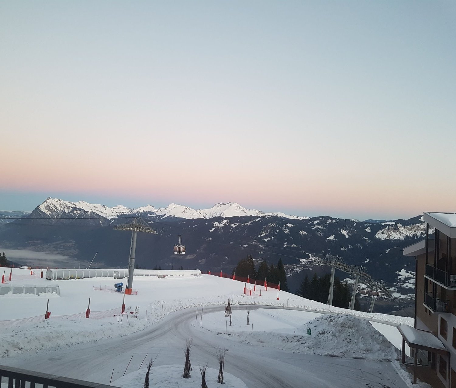 Dawn over snow-capped mountains, seen from Club Med Grand Massif, with a gondola crossing the valley
