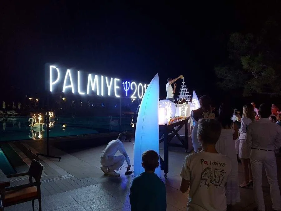 Soirée blanche de nuit au Club Med Palmiye (Turquie), avec l’enseigne lumineuse « PALMIYE » et une pyramide de coupes de champagne
