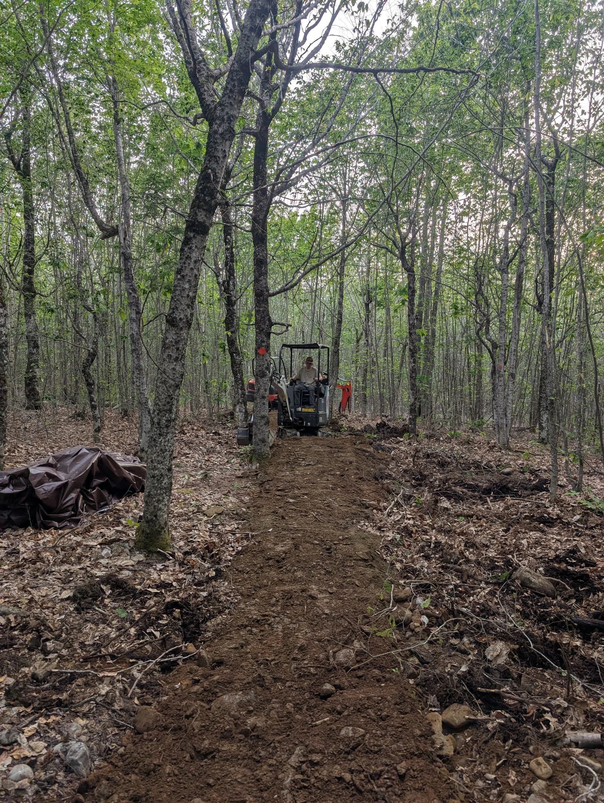 a trail building driving an excavator shapes a lift and tilt style hiking trail
