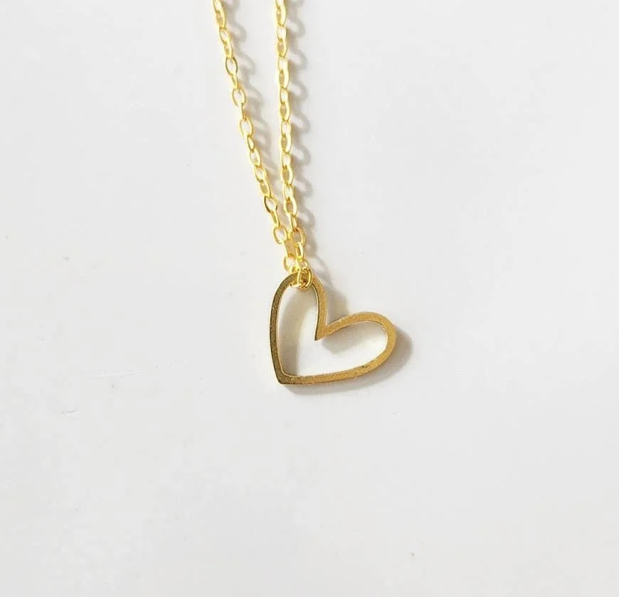 Gold-tone open heart pendant necklace on a delicate chain, photographed on a neutral background.