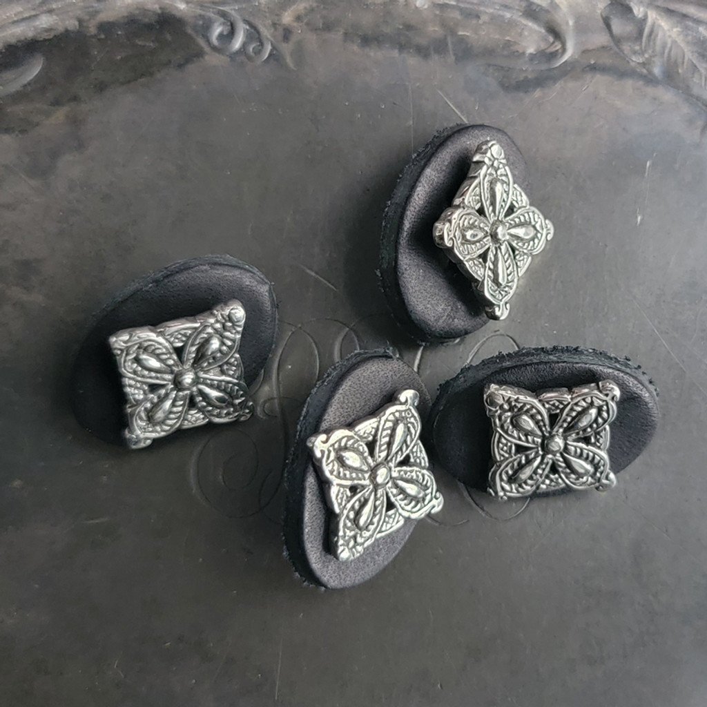 Antique-silver square floral filigree metal button displayed on black felt