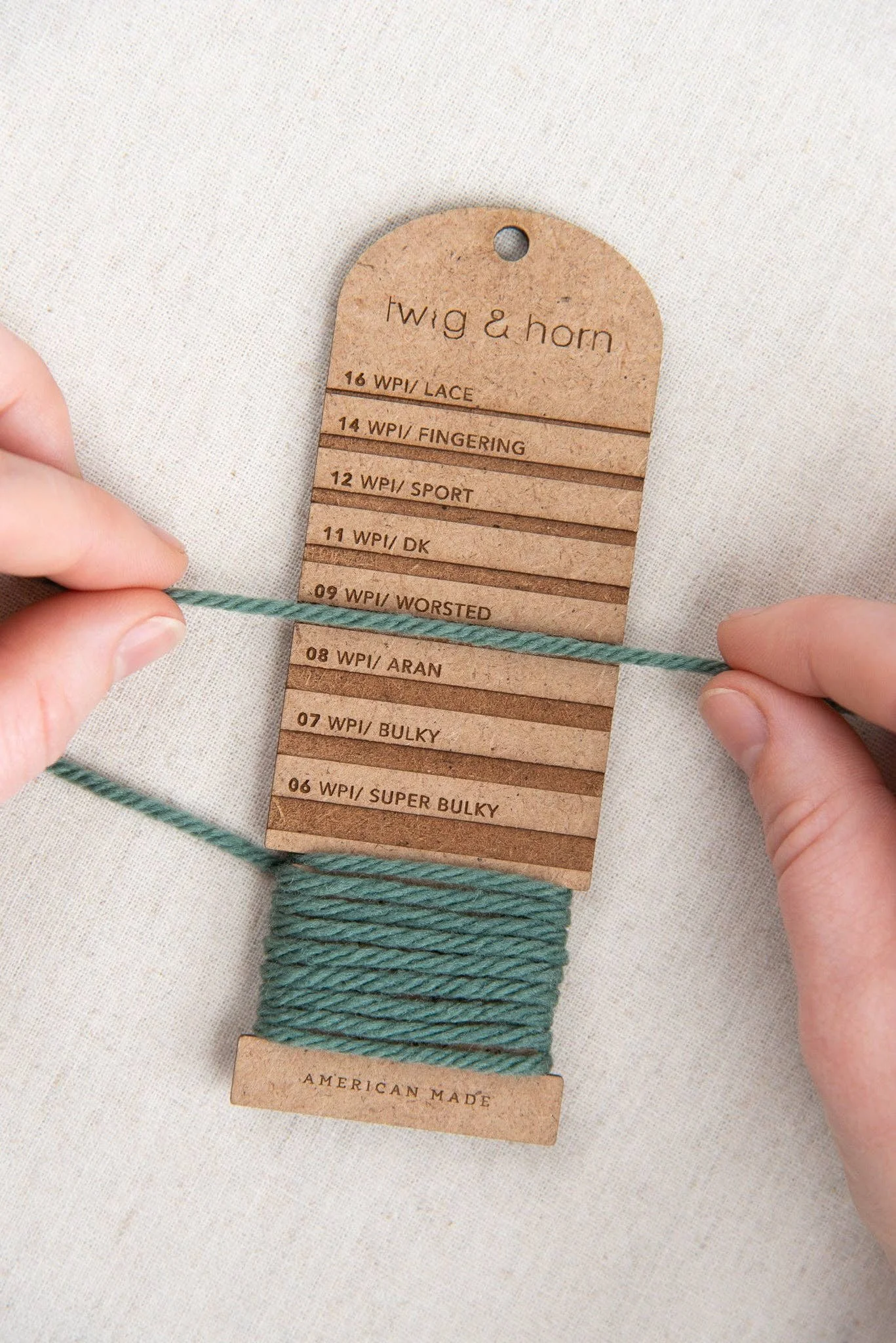 Hands using a wraps-per-inch tool to measure yarn thickness for gauge and yarn weight.