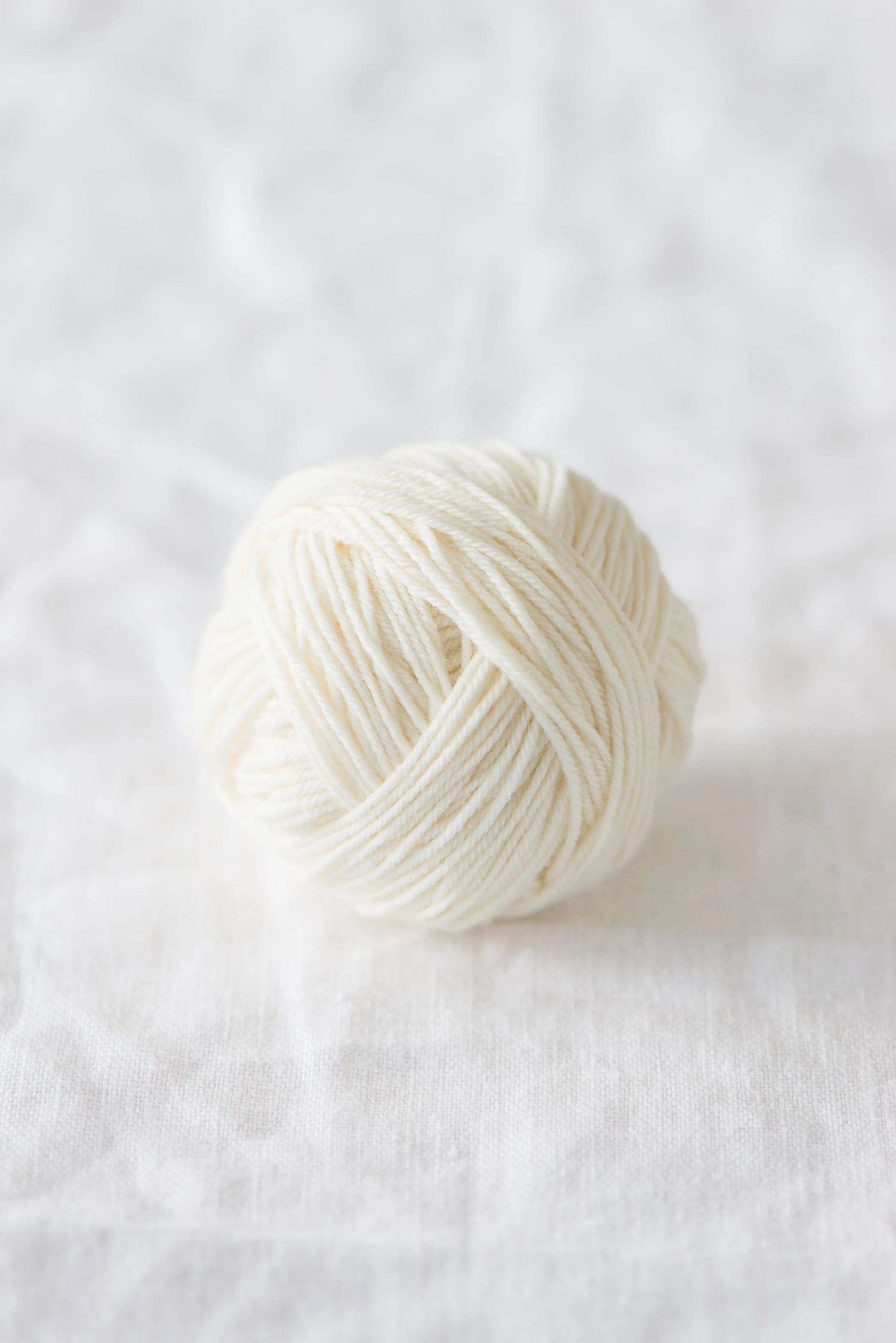 Cream-colored superwash merino fingering yarn ball for clean stitch definition and versatile projects.