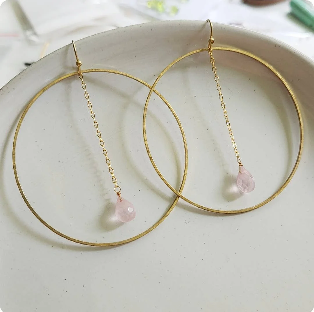Gold-tone hoops with a fine chain and rose quartz drop, shown close-up.
