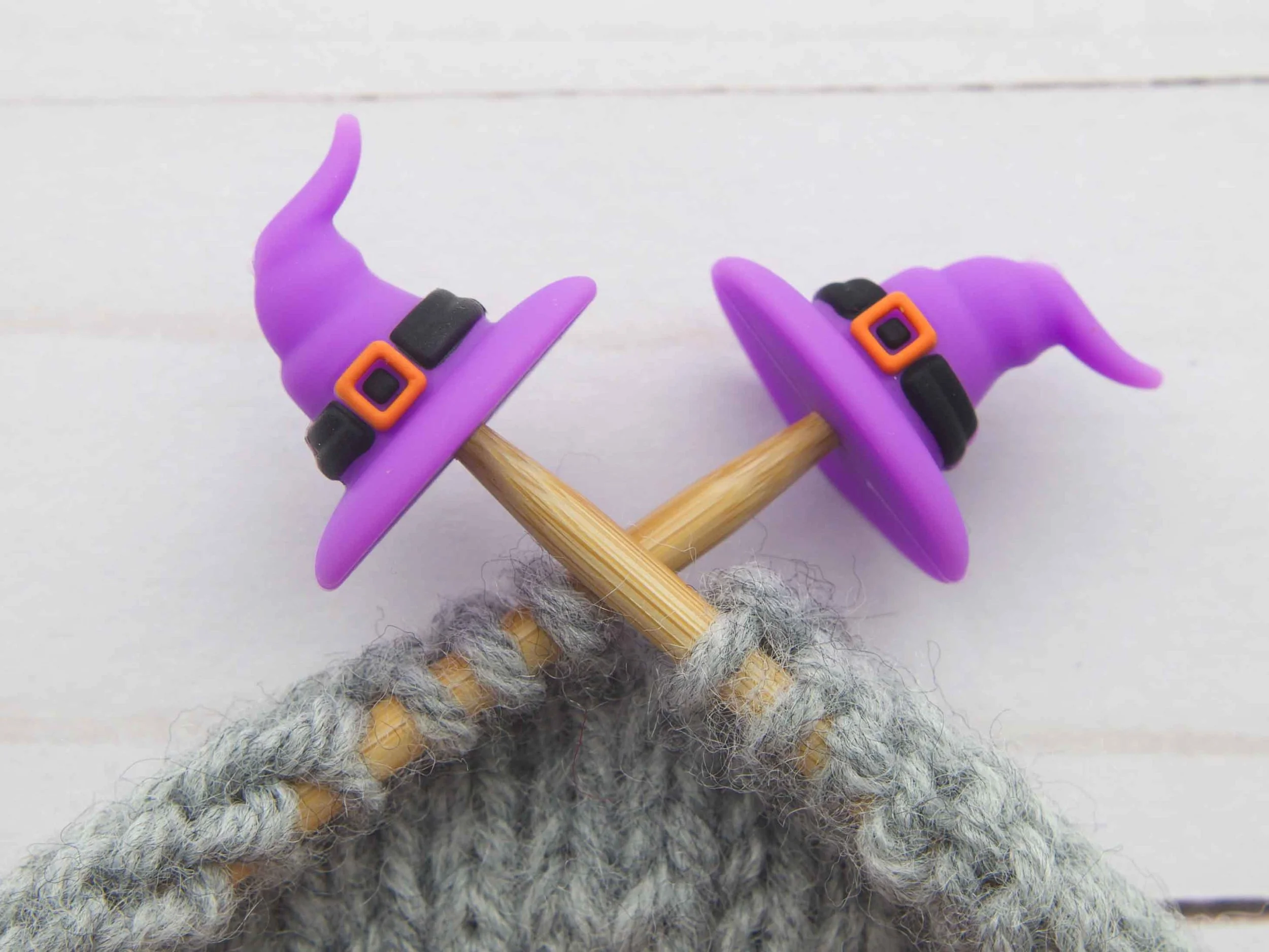 Purple witch-hat stitch stoppers on crossed bamboo needles with gray knitting